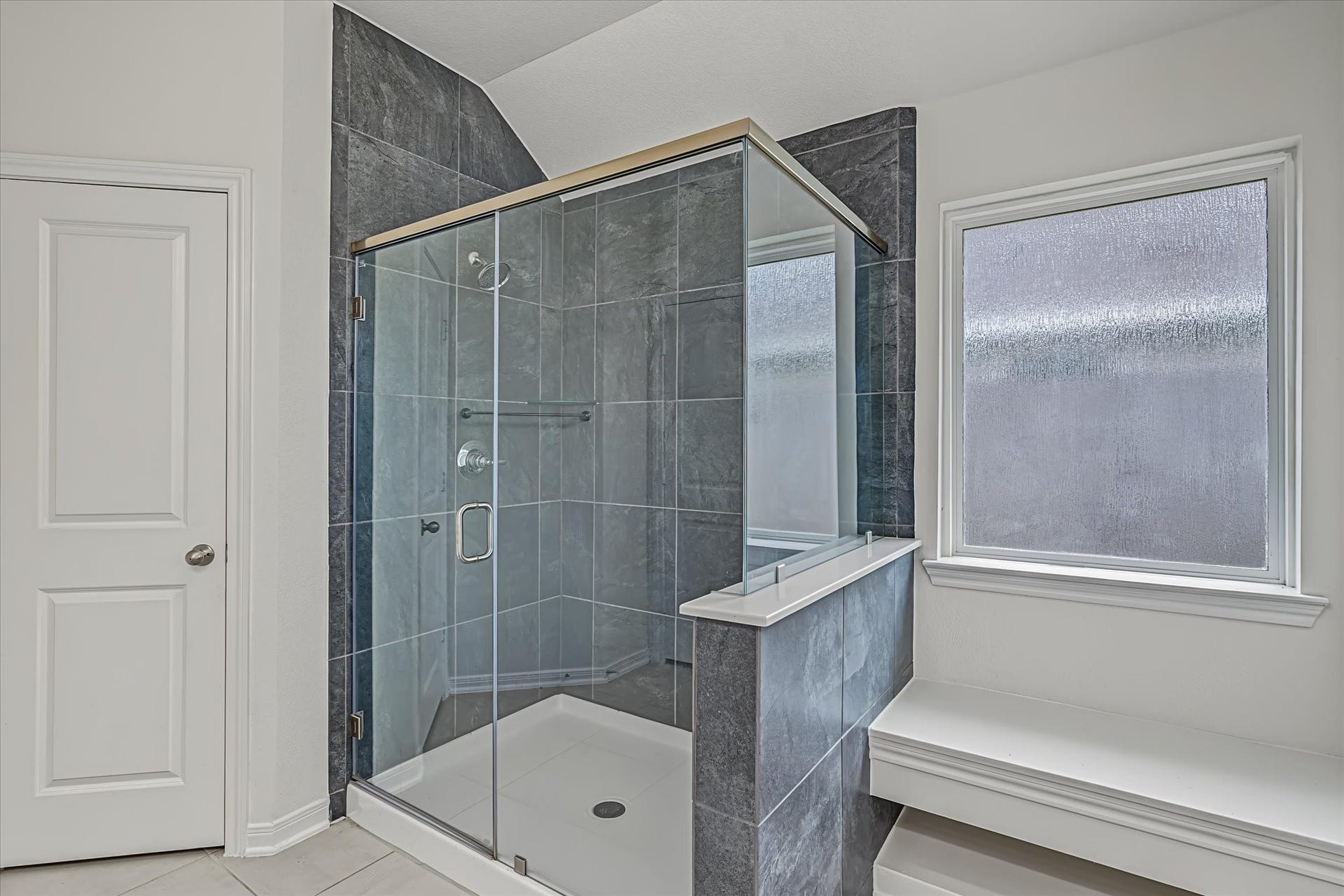 9607 Bright Song Lane, Houston, TX 77078 Modern Primary bathroom featuring a sleek glass-enclosed shower with elegant dark tiling and a large frosted window for natural light and privacy.