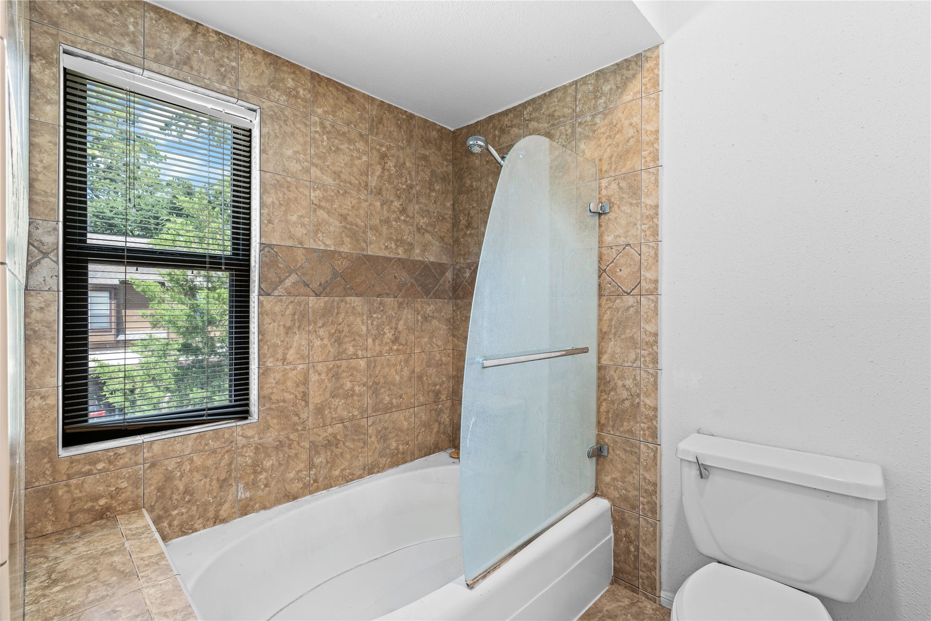 11711 Memorial Drive, #593, Houston, TX 77024 The primary bath features a fully tiled tub and shower surround, complemented by natural light from a nearby window.
