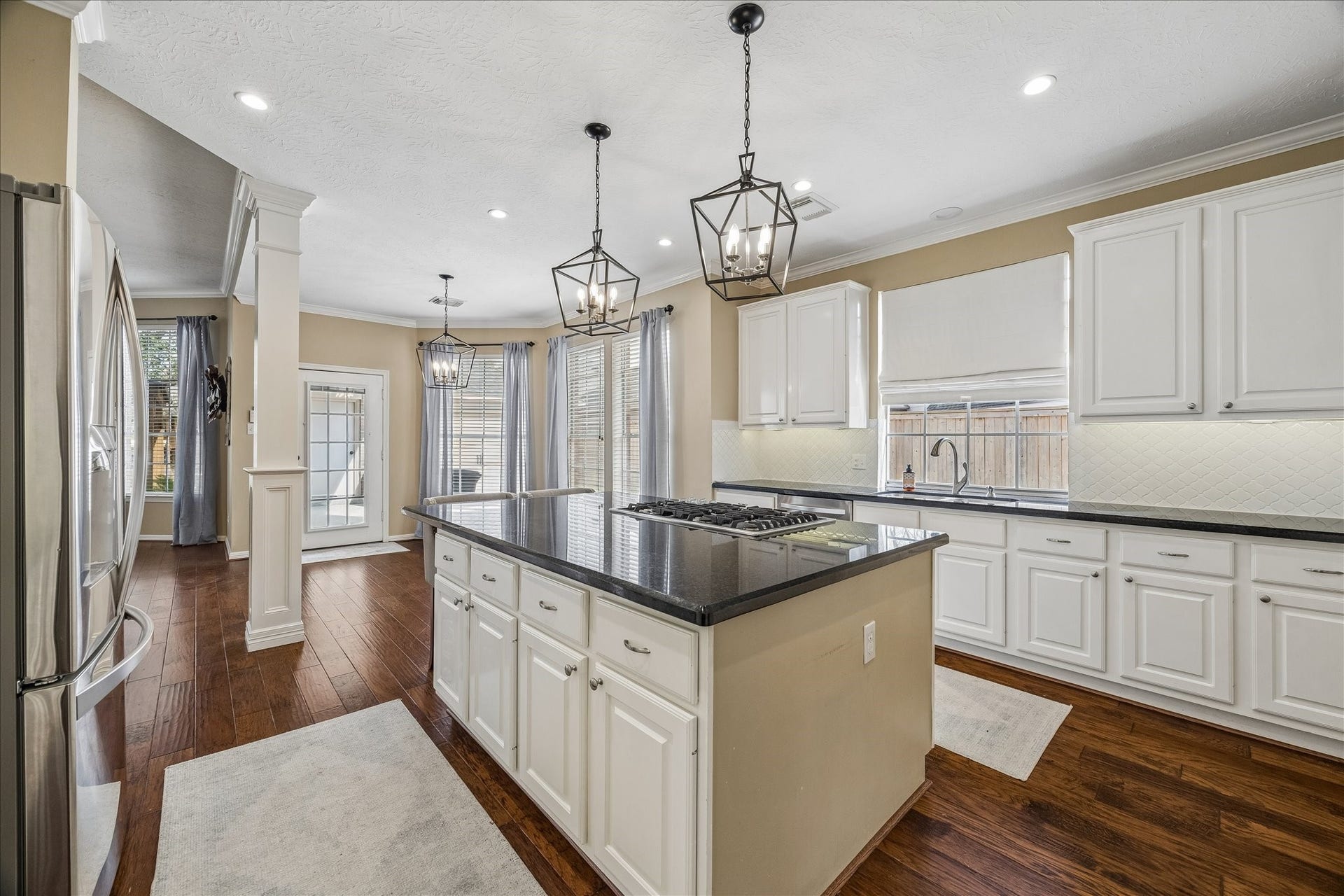 5310 Summerland Ridge Court, Houston, TX 77041 This kitchen features a spacious, open layout with elegant pendant lighting and ample natural light. It includes a large island with a stove, white cabinetry, and dark countertops. Hardwood floors and modern stainless steel appliances complete the look.