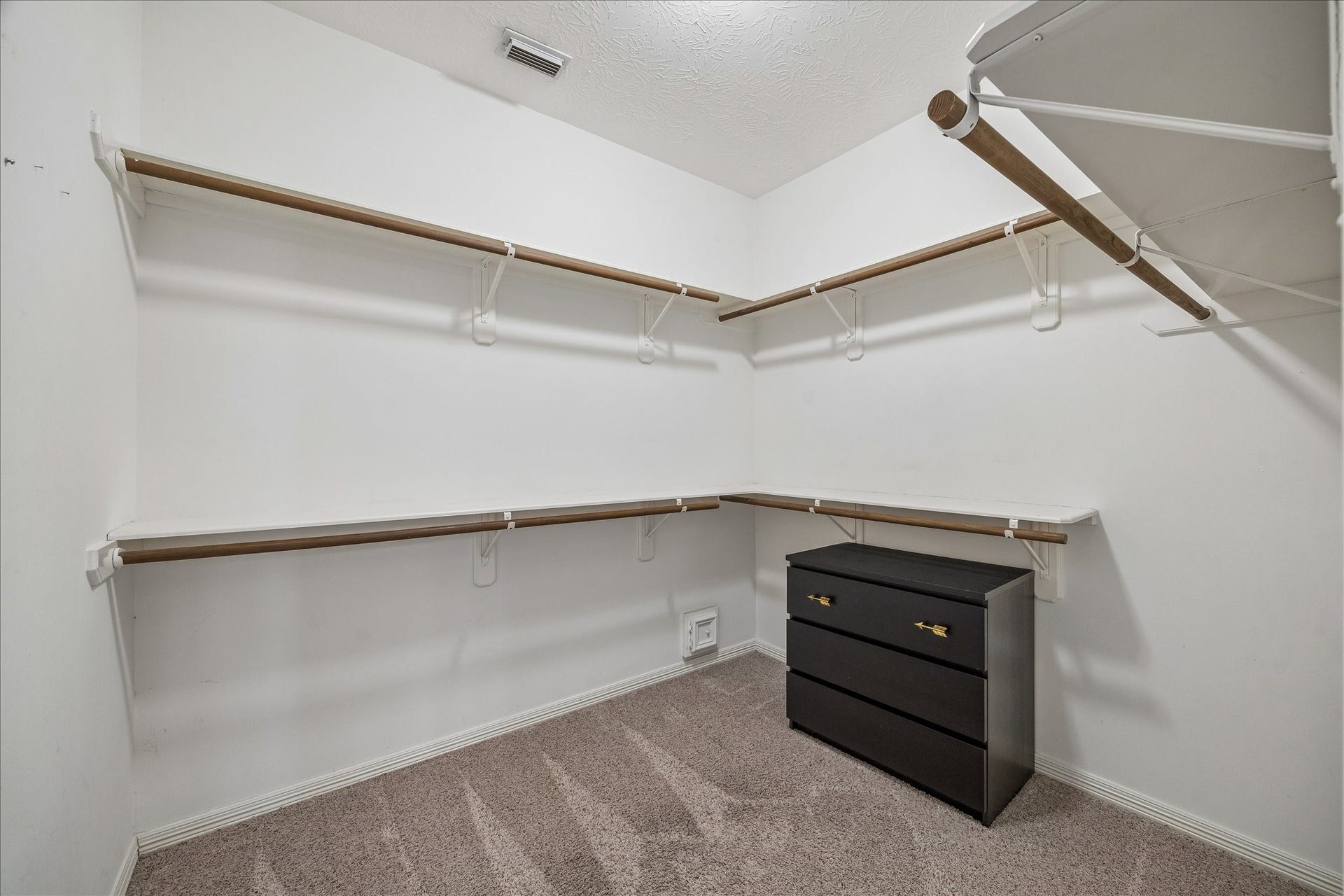 5310 Summerland Ridge Court, Houston, TX 77041 This photo shows a spacious walk-in closet with multiple wooden shelves and hanging rods for ample storage. The closet features neutral carpeting and includes a black dresser for additional organization.