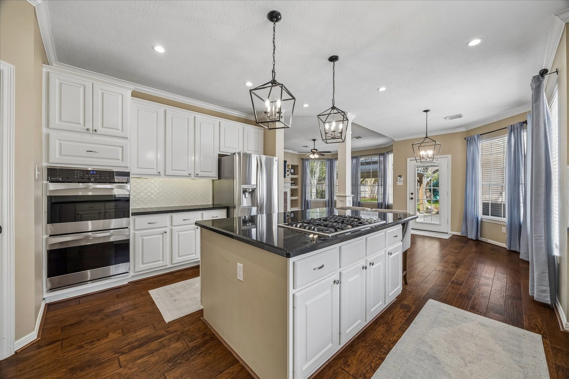 5310 Summerland Ridge Court, Houston, TX 77041 This spacious kitchen features elegant white cabinetry, a large island with a cooktop, modern stainless steel appliances, and stylish pendant lighting. The open layout flows into the dining area, enhanced by large windows and hardwood floors, creating a bright and inviting atmosphere.