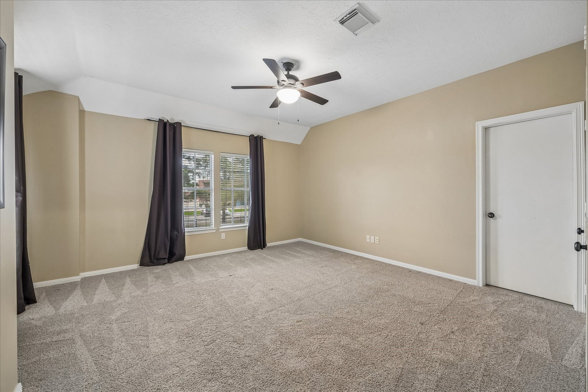 5310 Summerland Ridge Court, Houston, TX 77041 This spacious bedroom features neutral walls, a ceiling fan, and large windows with dark curtains, offering plenty of natural light.