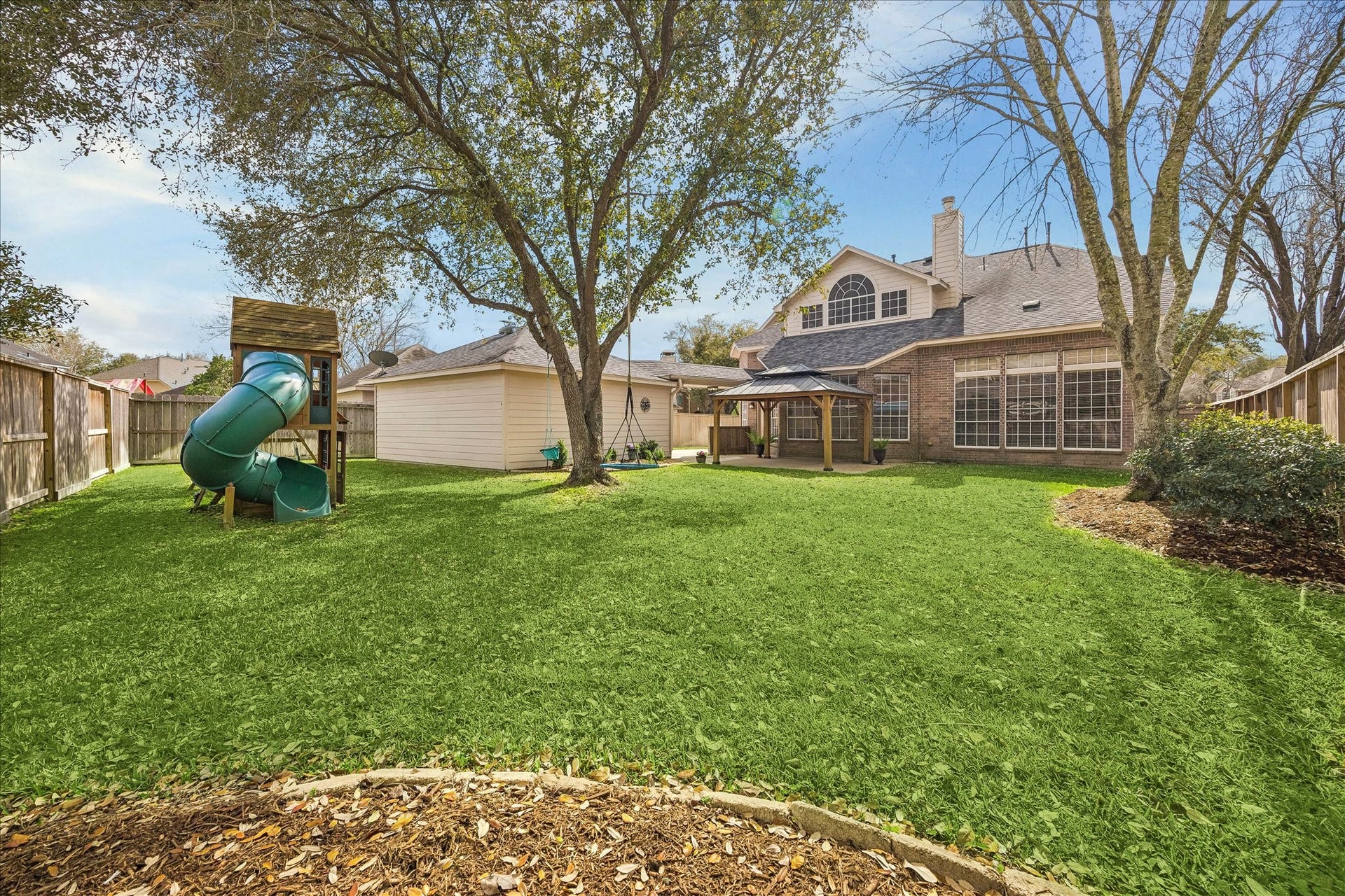 5310 Summerland Ridge Court, Houston, TX 77041 This spacious backyard features lush greenery, a playground set, and a charming gazebo, perfect for family activities and outdoor relaxation. The house has large windows, enhancing natural light.