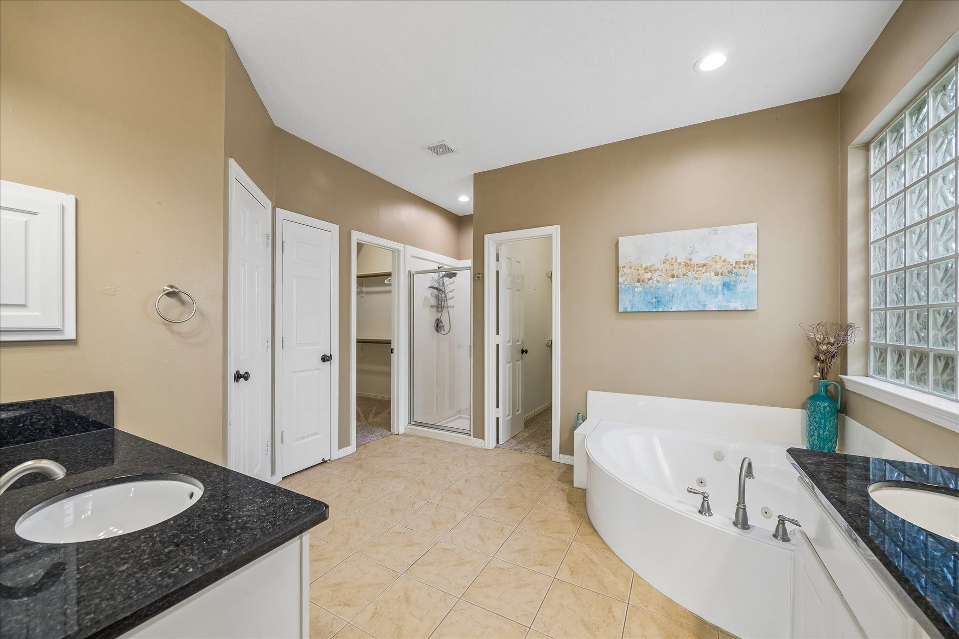 5310 Summerland Ridge Court, Houston, TX 77041 This spacious bathroom features dual sinks with granite countertops, a corner jetted tub, and a separate walk-in shower. It has a neutral color palette, tile flooring, and ample natural light from the glass block window.