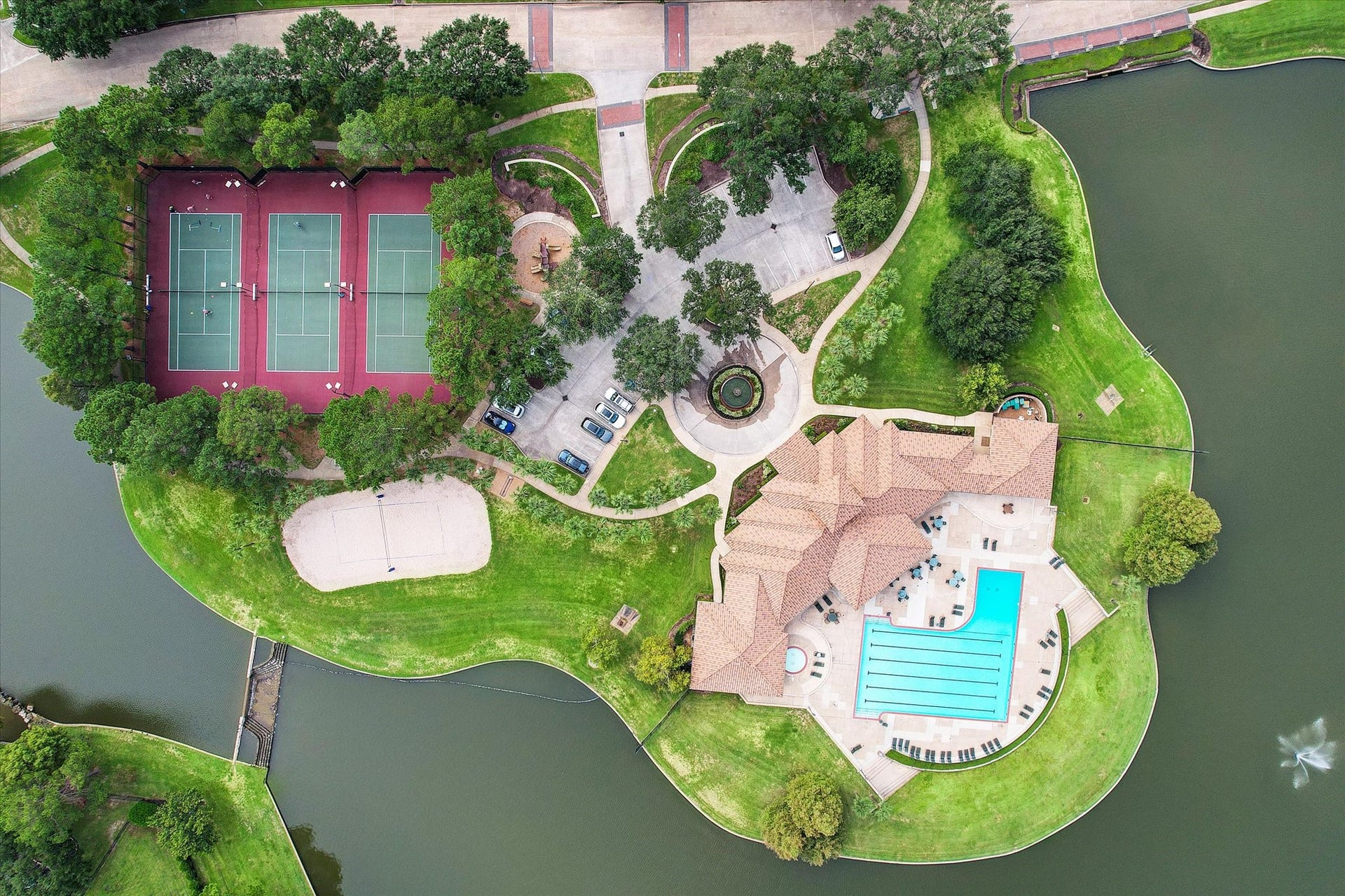 5310 Summerland Ridge Court, Houston, TX 77041 This aerial view showcases a scenic property featuring a large swimming pool, tennis courts, lush greenery, and a charming waterway. Ideal for active living and relaxation.