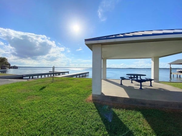 12195 N Lake Vista Drive, Willis, TX 77318 Enjoy serene outdoor living with this spacious, covered patio overlooking lush greenery, just steps away from a convenient boat ramp for endless water adventures.