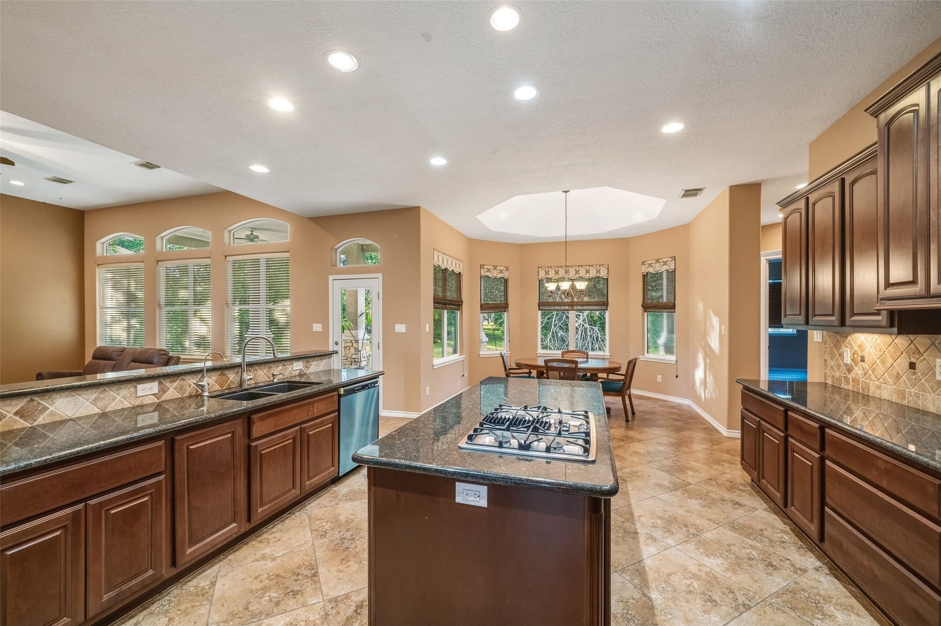 12195 N Lake Vista Drive, Willis, TX 77318 Spacious living area with a cozy stone fireplace, elegant tile flooring, and an open layout leading to a modern kitchen with rich wooden cabinetry.