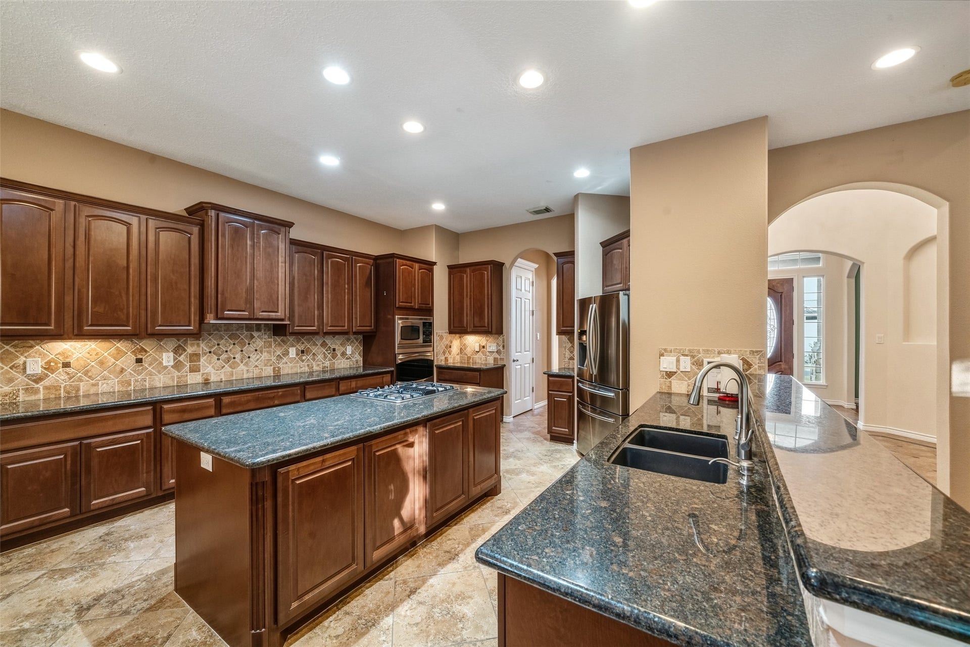 12195 N Lake Vista Drive, Willis, TX 77318 Spacious living area with tiled flooring, a stone fireplace, and abundant natural light from large arched windows, seamlessly flowing into an open kitchen and dining space.