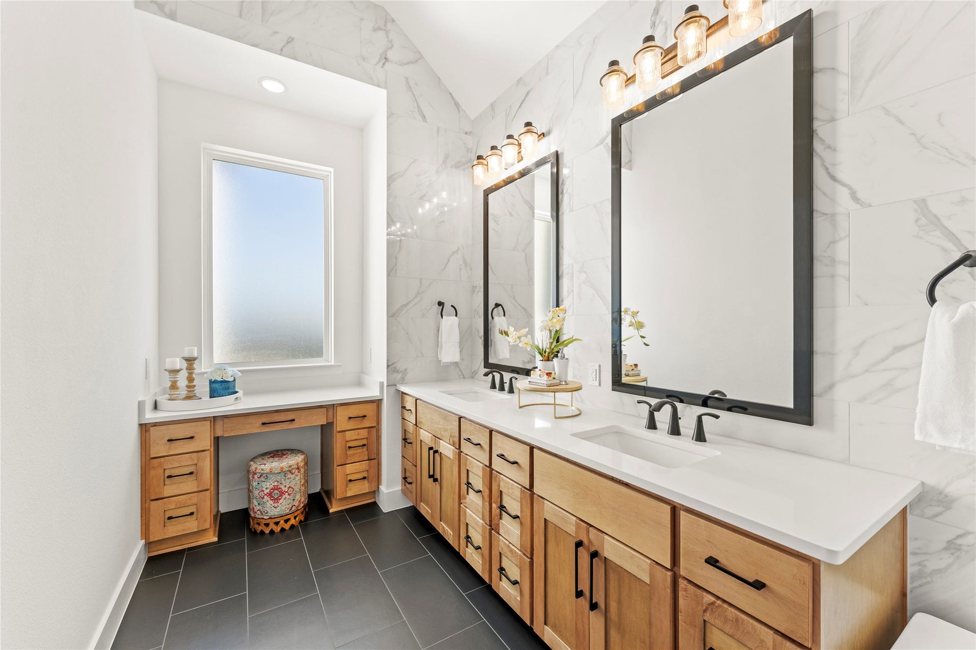 1934 Pleasant Grove Drive, Missouri City, TX 77459 Step into your private spa-like oasis in this stunning primary en-suite bathroom! The space features a long, custom double vanity with warm wood cabinetry and a dedicated makeup station tucked perfectly under a bright window.