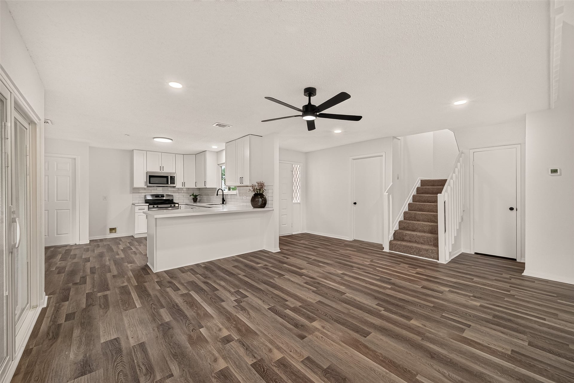 12747 Ashford Knoll Drive, Houston, TX 77082 Open-concept living area with sleek luxury vinyl plank floors, modern ceiling fan, and a bright kitchen featuring stainless steel appliances and an inviting breakfast bar.