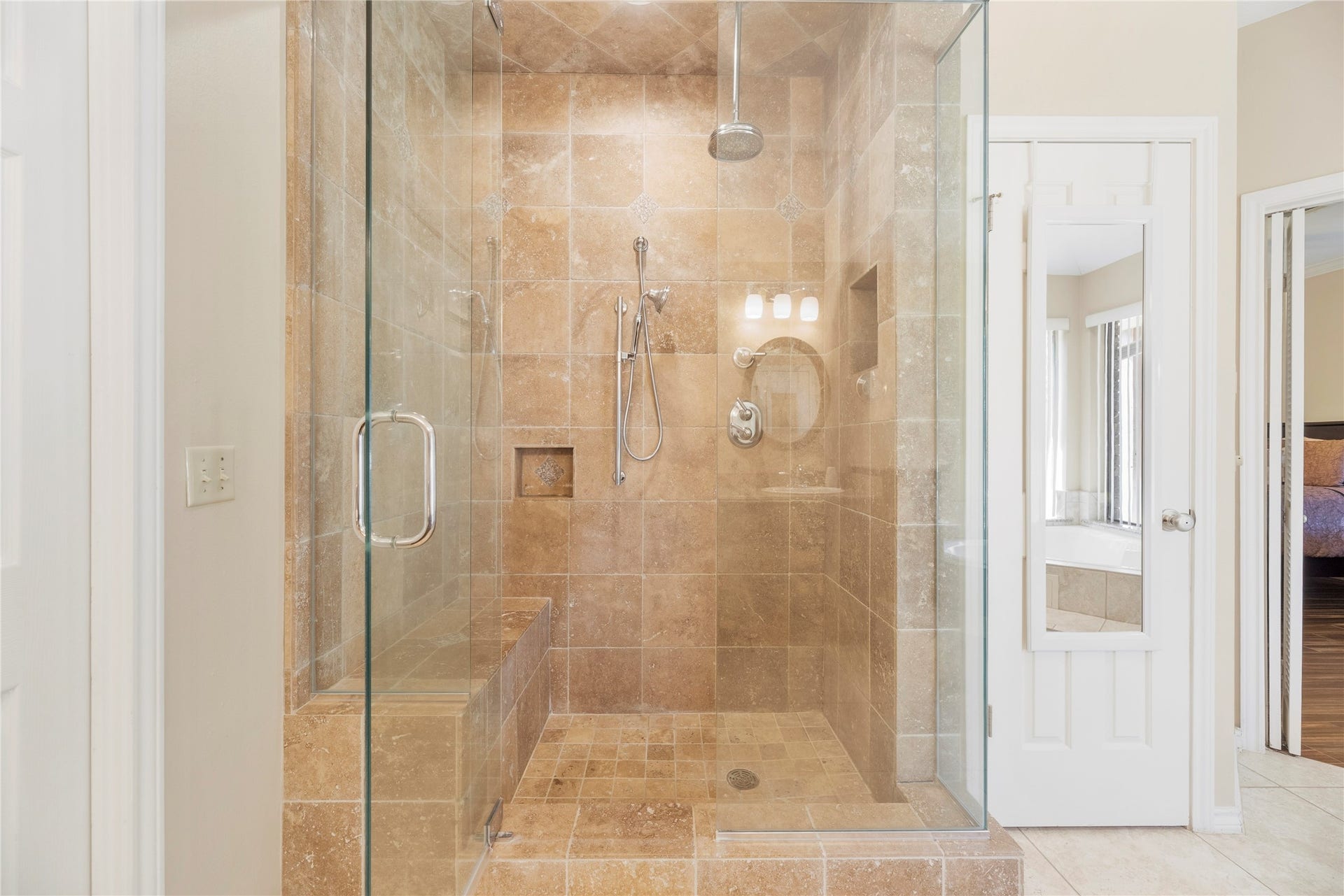 Luxurious frameless glass inclosed primary shower with elegant tile work and modern fixtures including a rain shower head.