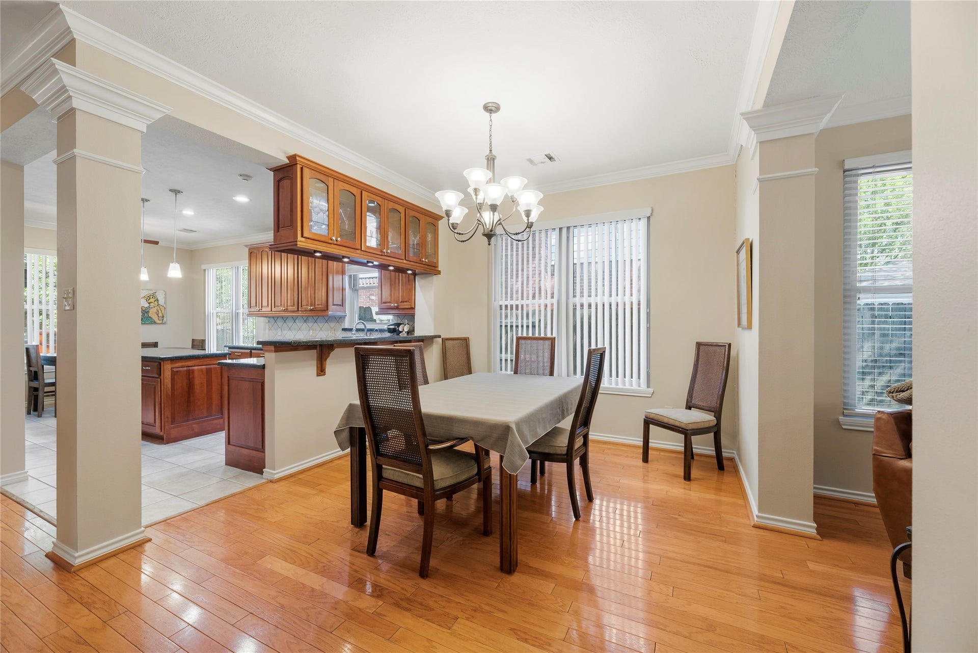 Elegant dining area with warm wood flooring and a stylish chandelier, seamlessly connected to a modern kitchen and open to the family room.