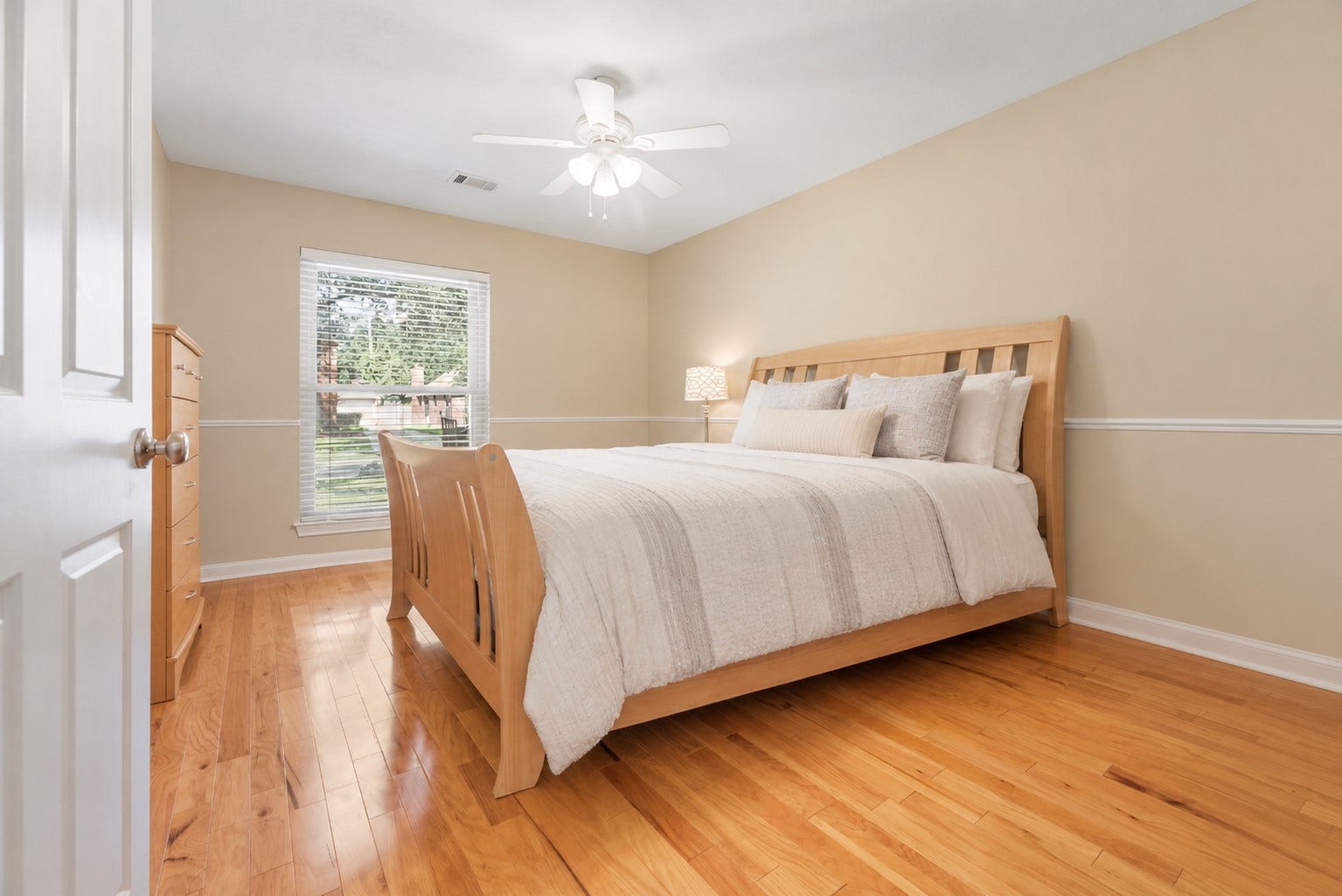 Cozy bedroom with warm wood flooring, chair railing, and a large window for natural light. **Virtually Staged**