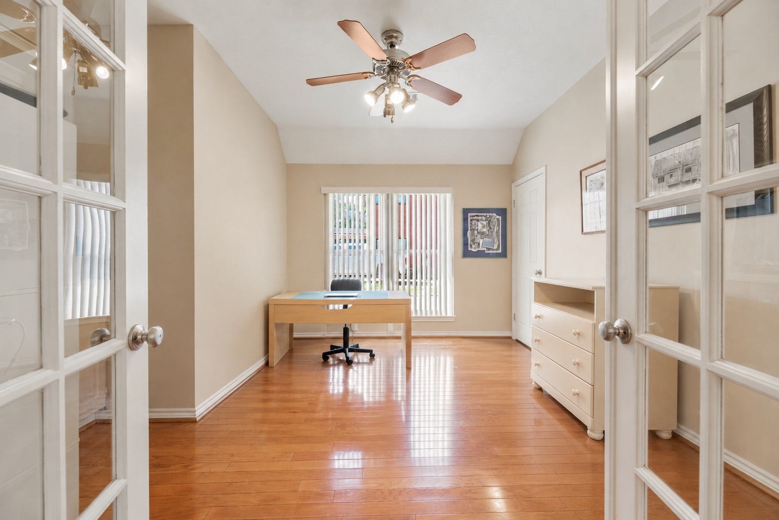 Bright home office with elegant French doors, a ceiling fan, and warm hardwood floors. **Virtually Staged**