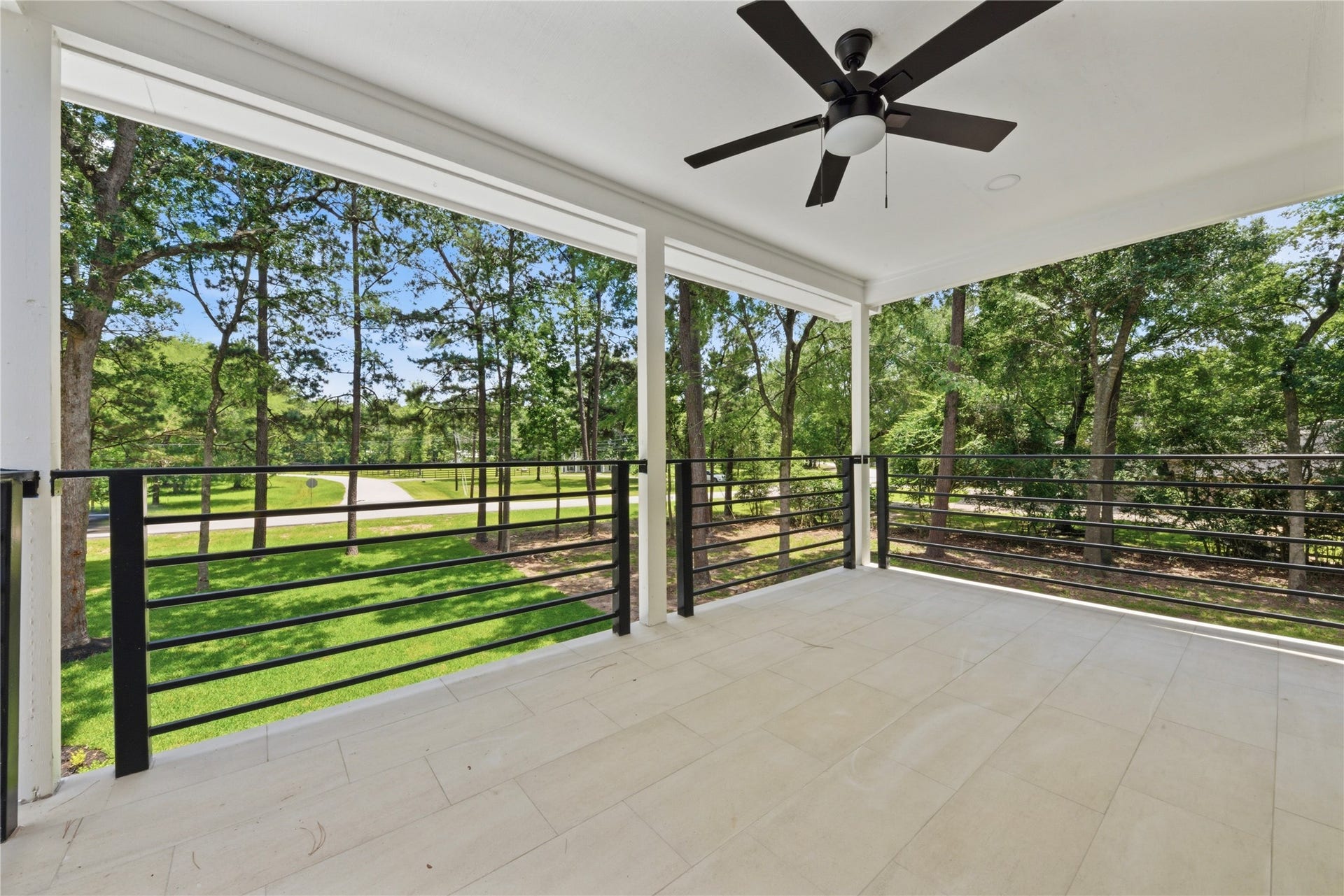 40203 Cimarron Way, Magnolia, TX 77354 Generous covered upper balcony off the 3rd-floor second primary suite. Features designer ceiling fan, horizontal black metal railing, tiled flooring, and serene treetop views of the wooded 1.67-acre lot. Perfect for morning coffee or evening sunsets.