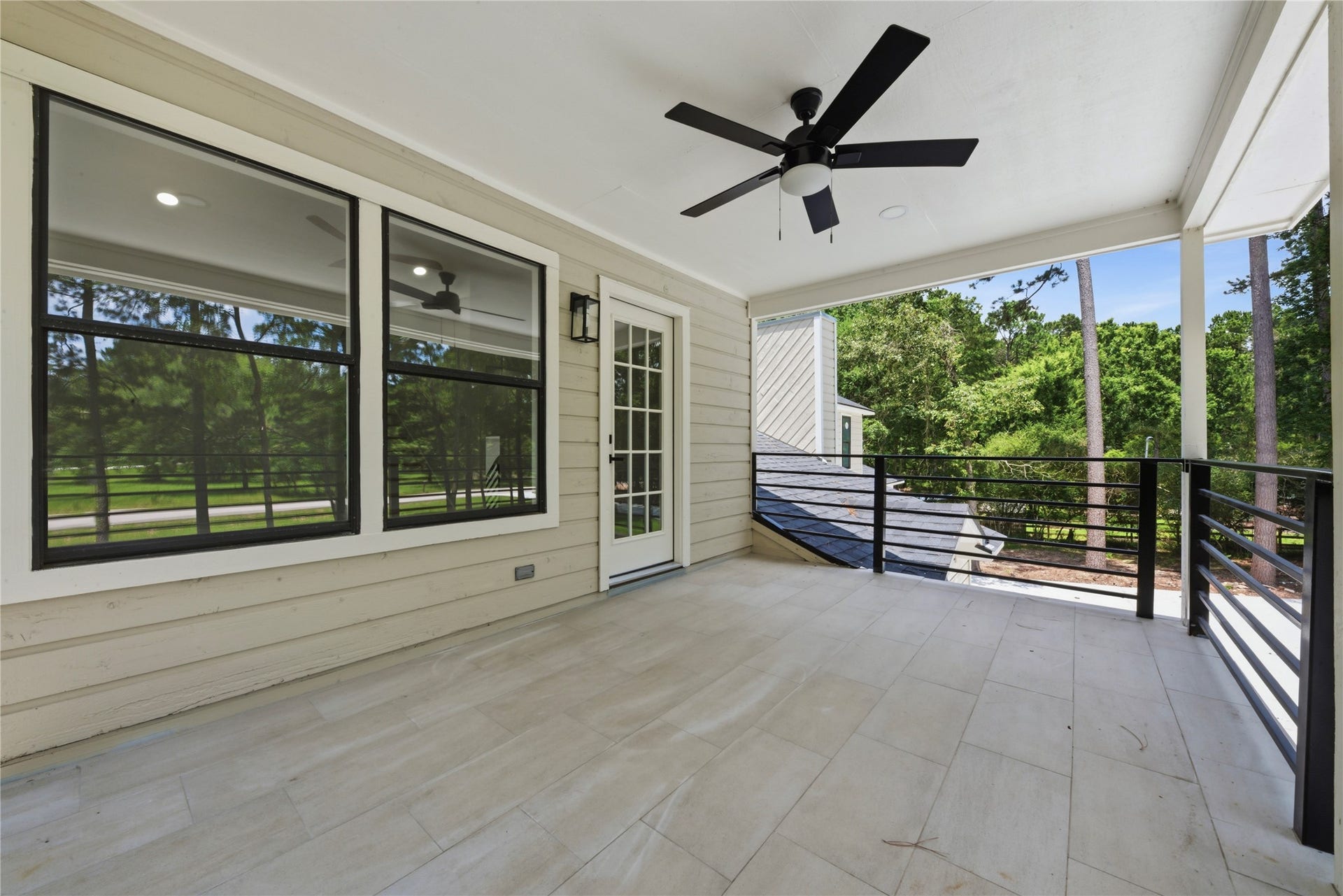 40203 Cimarron Way, Magnolia, TX 77354 Expansive covered upper balcony showing the rooftop view of the detached 3-car garage structure to the right. French door access from the second primary suite. Horizontal black metal rail with treeline beyond.