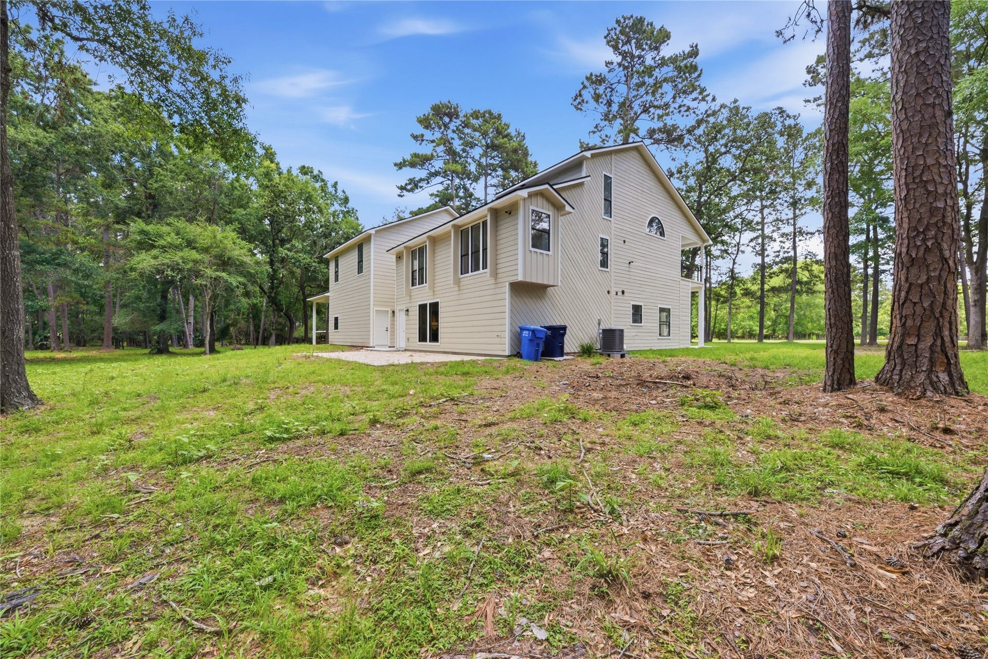 40203 Cimarron Way, Magnolia, TX 77354 Daytime view of the rear elevation showcasing the home's substantial profile, modern board-and-batten siding, and the scale of the surrounding wooded lot. AC units neatly tucked at the side.