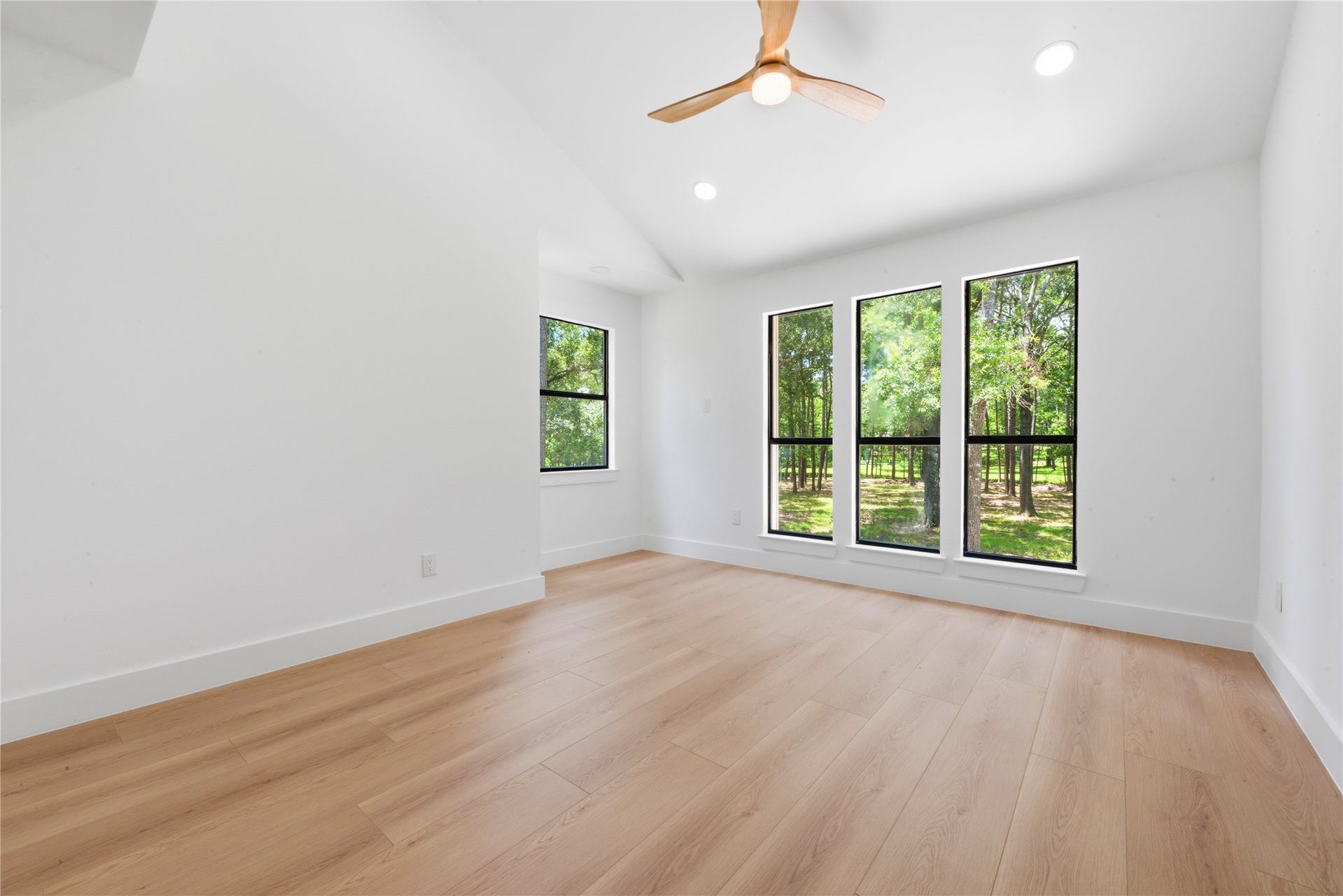 40203 Cimarron Way, Magnolia, TX 77354 Second upstairs bedroom with vaulted ceiling and designer ceiling fan. Floor-to-ceiling black-frame windows fill the space with natural light and frame the mature tree views.