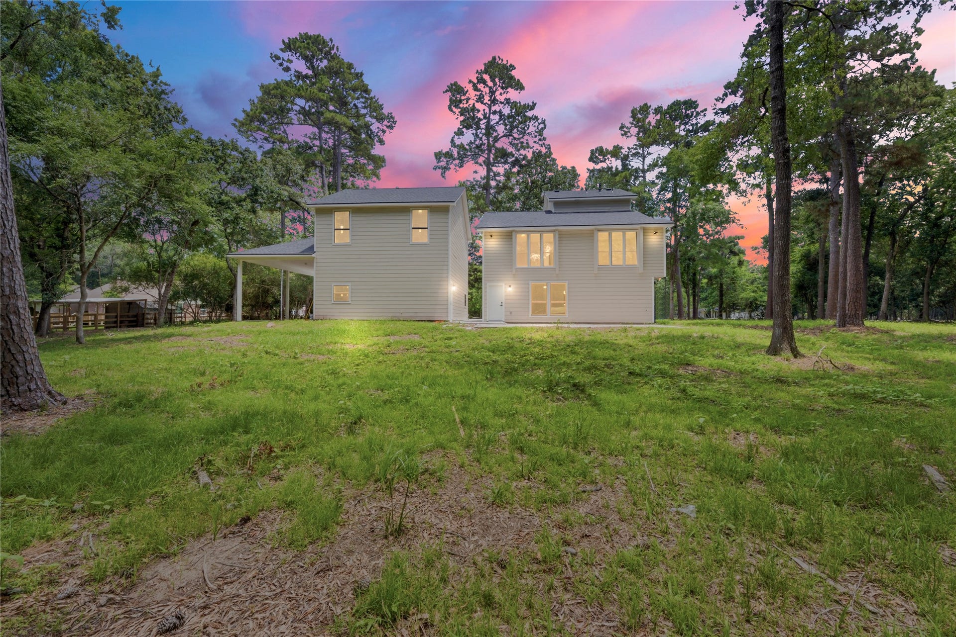 40203 Cimarron Way, Magnolia, TX 77354 Magical twilight view of the rear elevation of the main home, glowing windows showcasing the great room and second primary suite. Set on 1.67 wooded acres in coveted Cimarron Country. Mature pines and natural privacy frame the property.