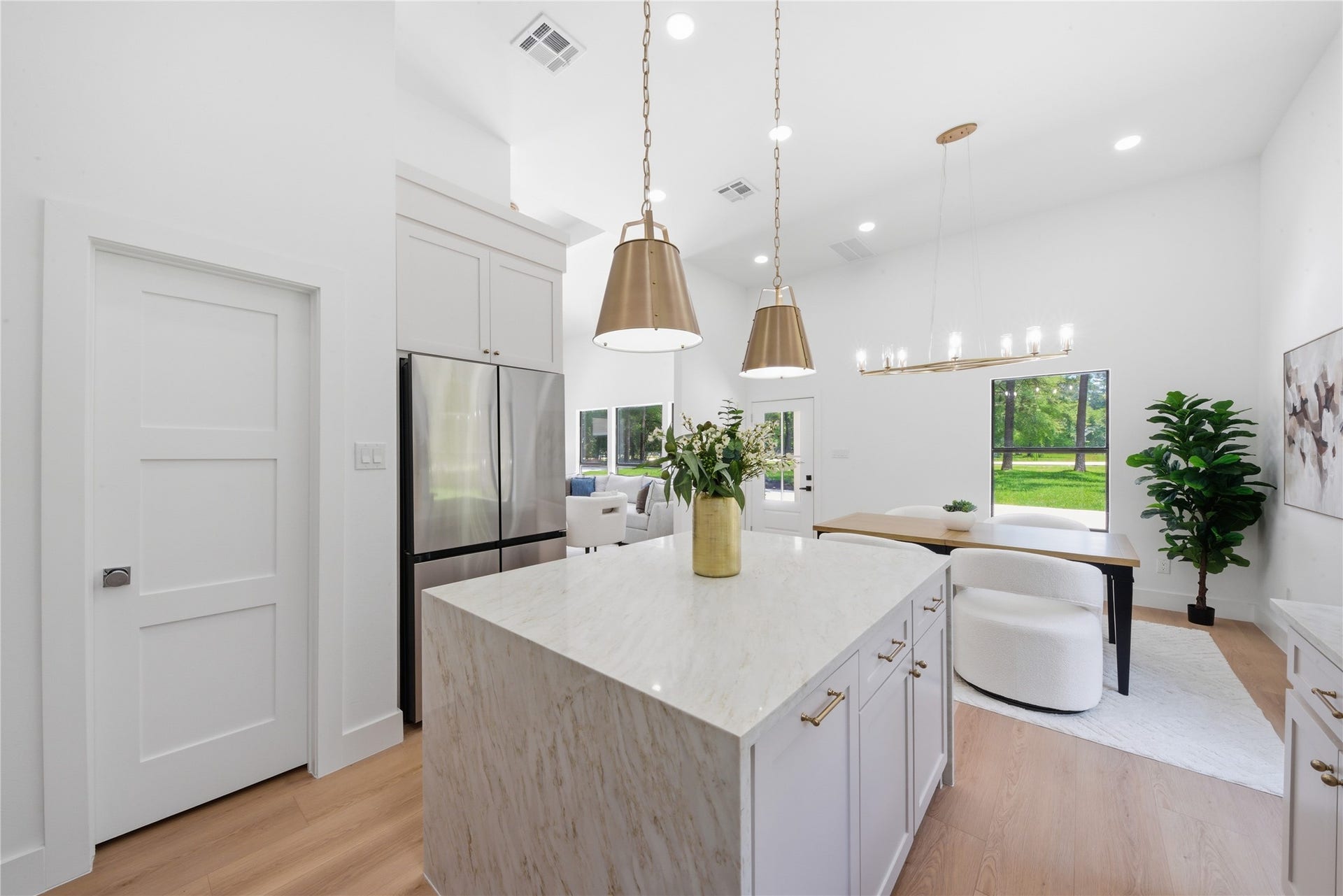 40203 Cimarron Way, Magnolia, TX 77354 Open-concept kitchen opening to the living and breakfast areas. Soft-close custom cabinetry conceals a walk-in pantry door (left). Refrigerator included. Statement chandeliers and brass pendants illuminate the space.