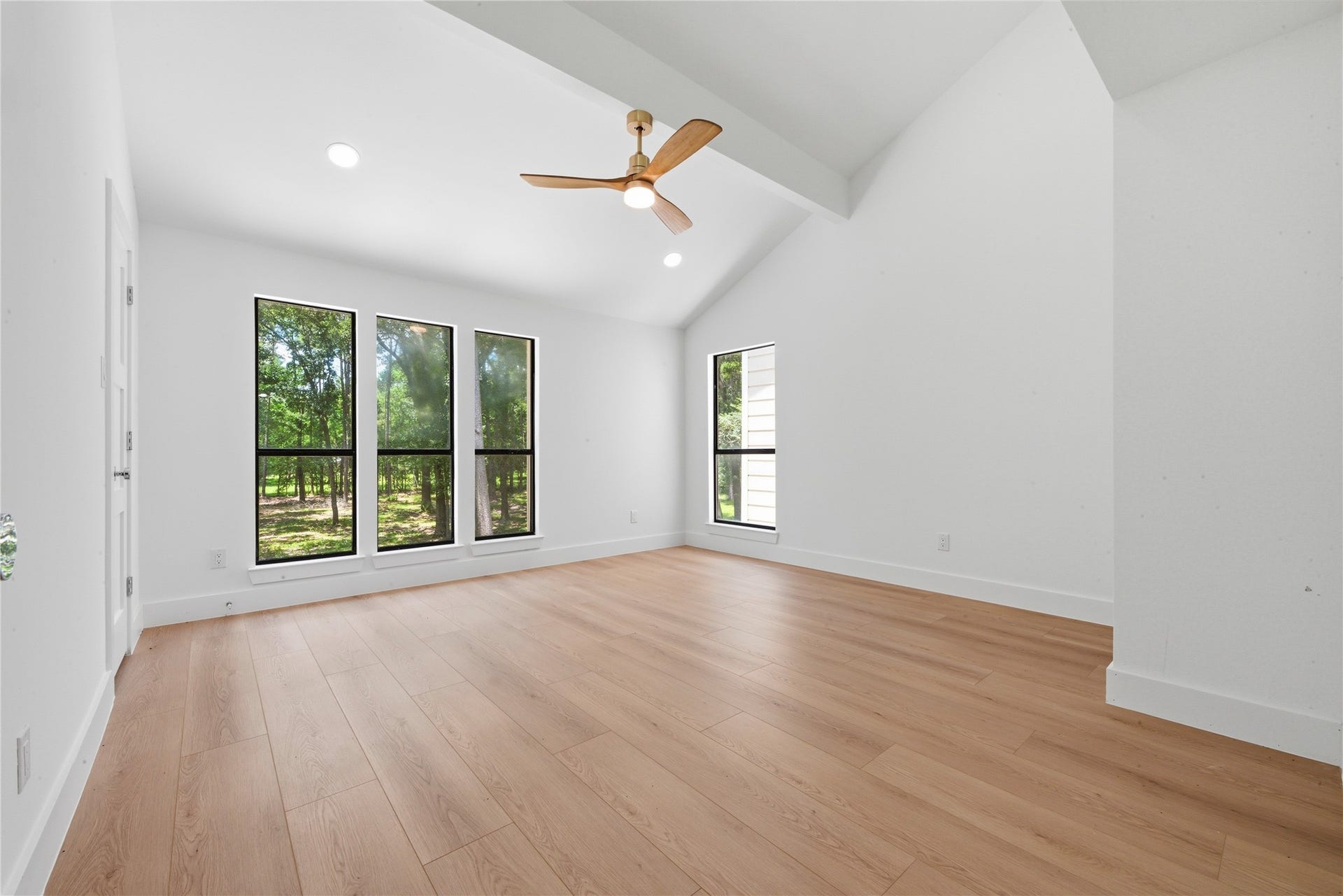 40203 Cimarron Way, Magnolia, TX 77354 Light-filled secondary bedroom with vaulted ceiling, designer ceiling fan, wide-plank floors, and trio of oversized black-frame windows showcasing wooded acreage views. Generous footprint with closet.