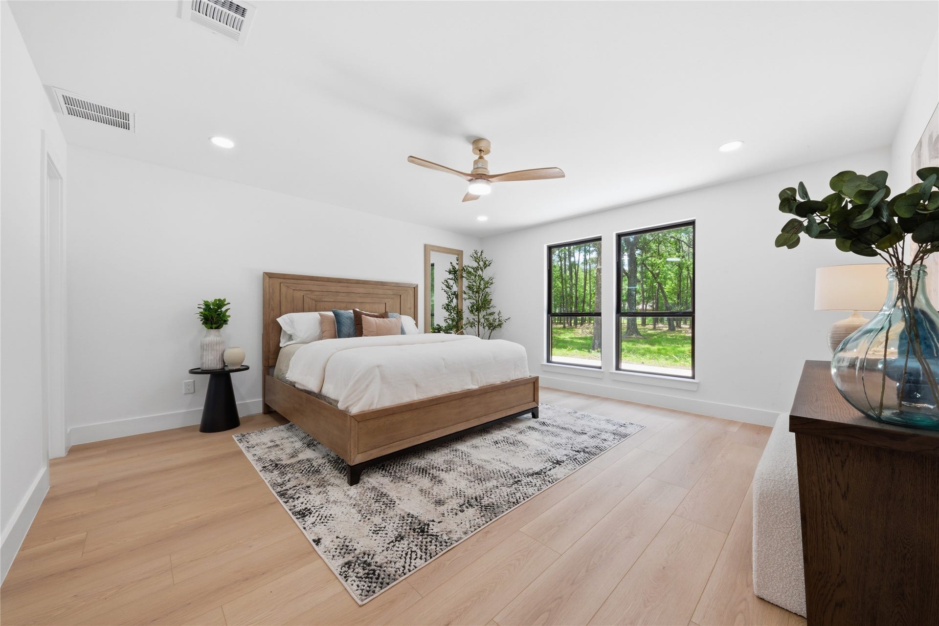 40203 Cimarron Way, Magnolia, TX 77354 Spacious first-floor primary suite with wide-plank white oak floors, designer ceiling fan, oversized windows framing wooded backyard views, and direct ensuite access. Light-filled and serene retreat.