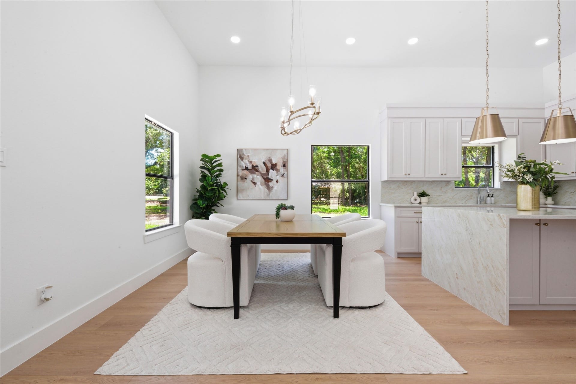 40203 Cimarron Way, Magnolia, TX 77354 Dining space flowing into the chef's kitchen featuring waterfall quartz island and brass pendant lighting. Vaulted ceilings, designer chandelier, and oversized windows frame views of the wooded acreage.