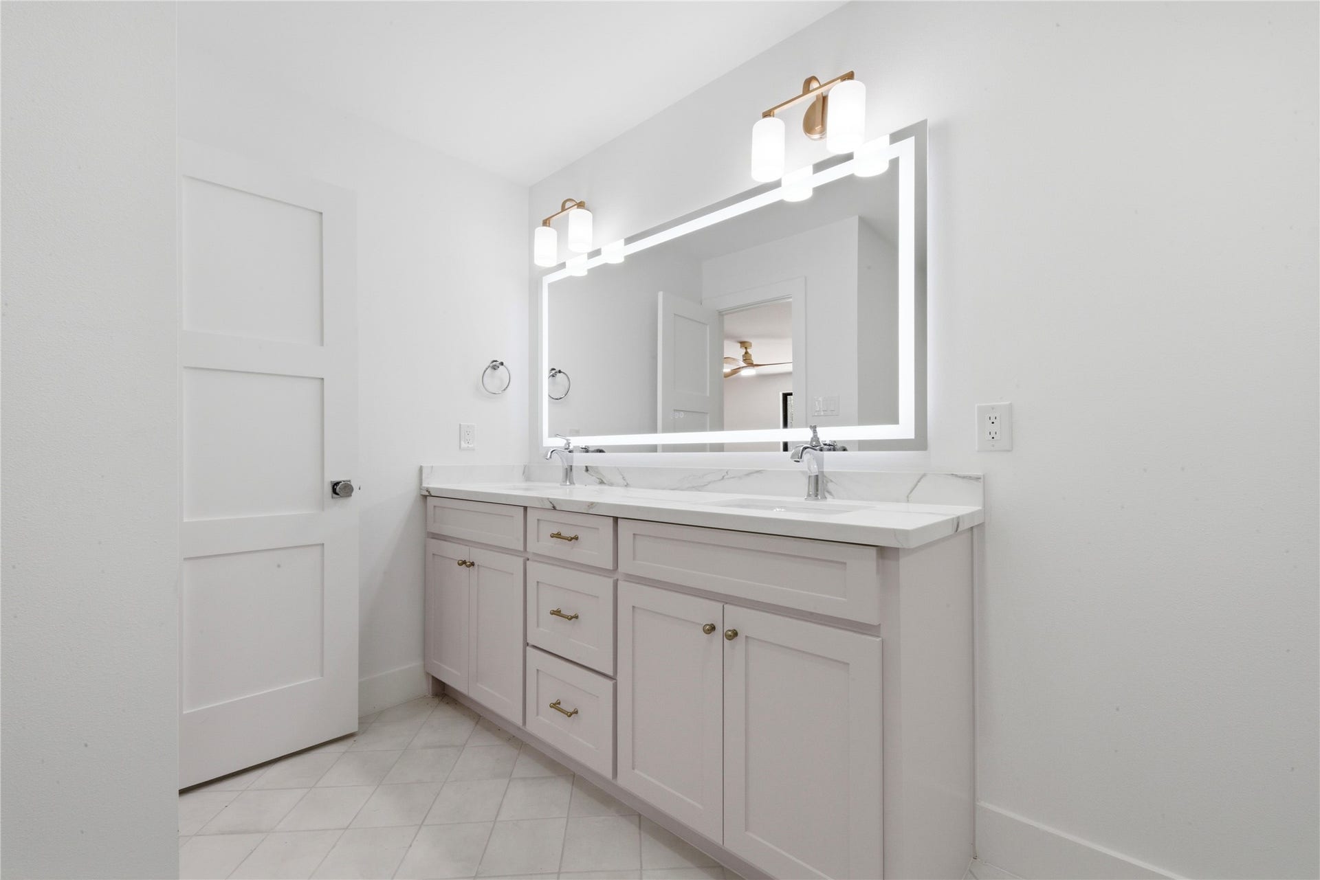 40203 Cimarron Way, Magnolia, TX 77354 Designer secondary bath featuring dual sinks with quartz waterfall counter, LED-backlit vanity mirror, brass sconces, custom shaker cabinetry with brass hardware, and tile flooring. Shared by the two upstairs secondary bedrooms.