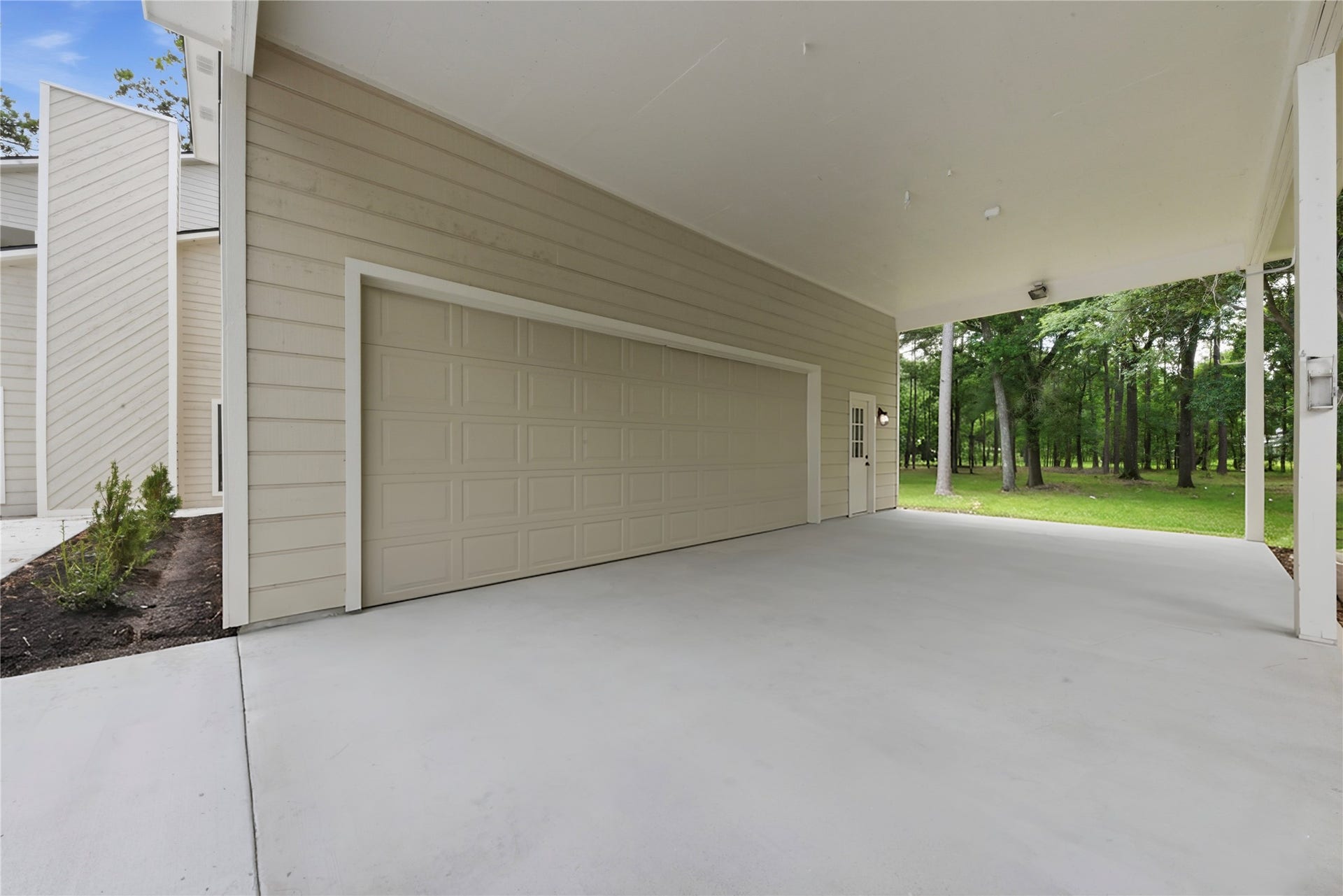 40203 Cimarron Way, Magnolia, TX 77354 Exterior view of the detached 3-car garage structure showing oversized garage door, fresh concrete drive, board-and-batten siding, and direct access to the surrounding 1.67 acres of wooded land. Easy turnaround and ample parking.