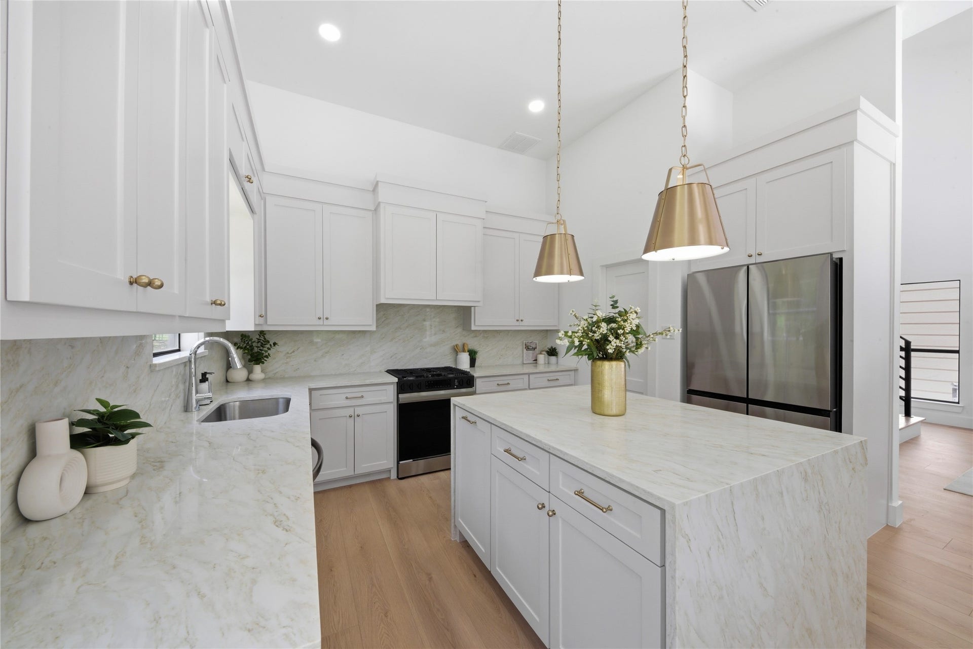 40203 Cimarron Way, Magnolia, TX 77354 Designer chef's kitchen featuring oversized waterfall quartz island, custom cream shaker cabinetry, brass cone pendants, stainless steel appliances, gas range, and quartz slab backsplash. Light wide-plank floors and brass hardware throughout.
