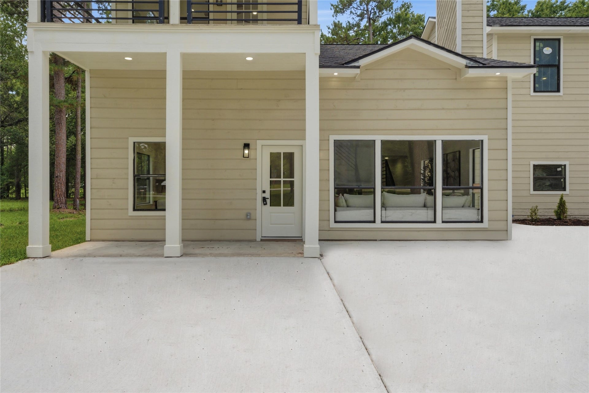 40203 Cimarron Way, Magnolia, TX 77354 Striking modern farmhouse facade featuring covered upper balcony, double-stack design, board-and-batten siding, and oversized picture windows showcasing the open-concept interior. Pristine concrete drive and walkway.