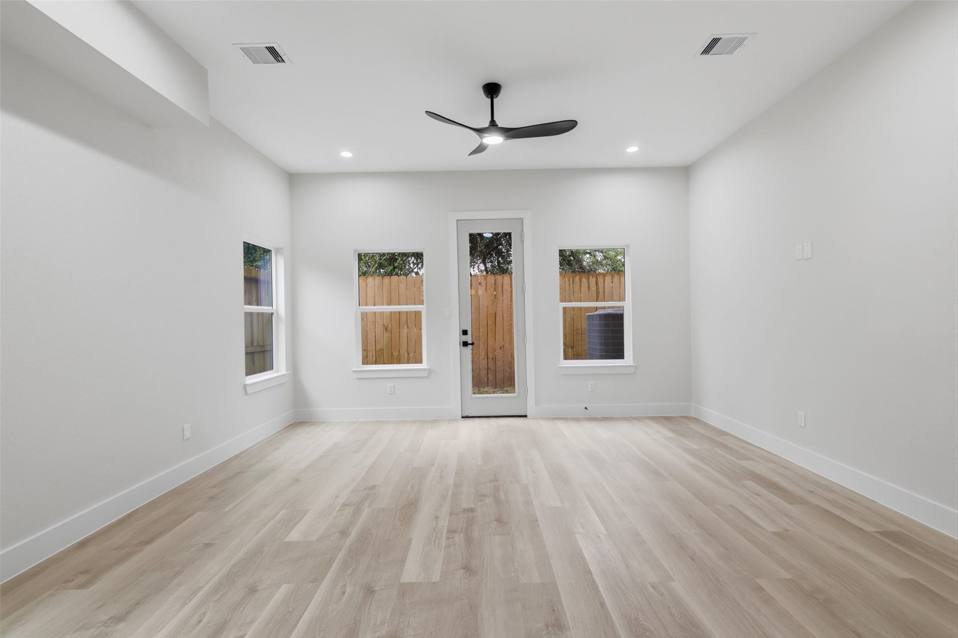 Bright and spacious living room featuring sleek LVP flooring, recessed lighting, and a modern ceiling fan, with direct access to a fenced backyard through a glass door.