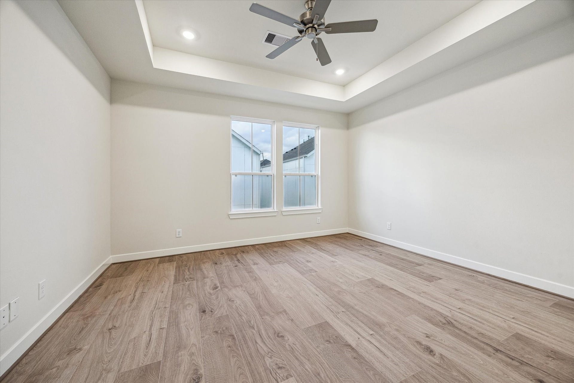 Large primary bedroom featuring a tray ceiling, recessed lighting, ceiling fan, and large windows for natural light.