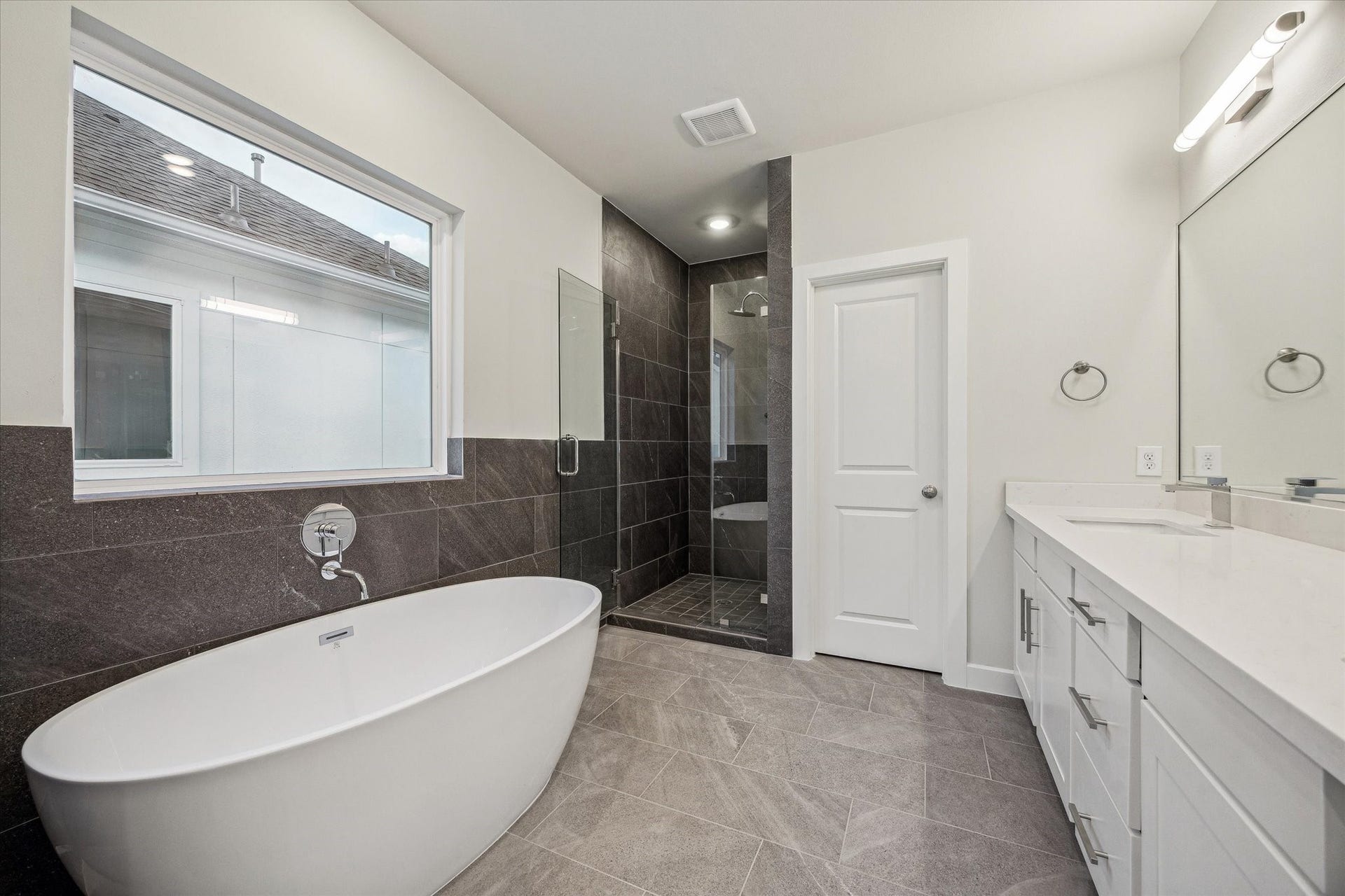 Primary bath featuring a freestanding soaking tub, glass-enclosed shower, white vanity cabinetry, modern fixtures, and a spacious, clean design.