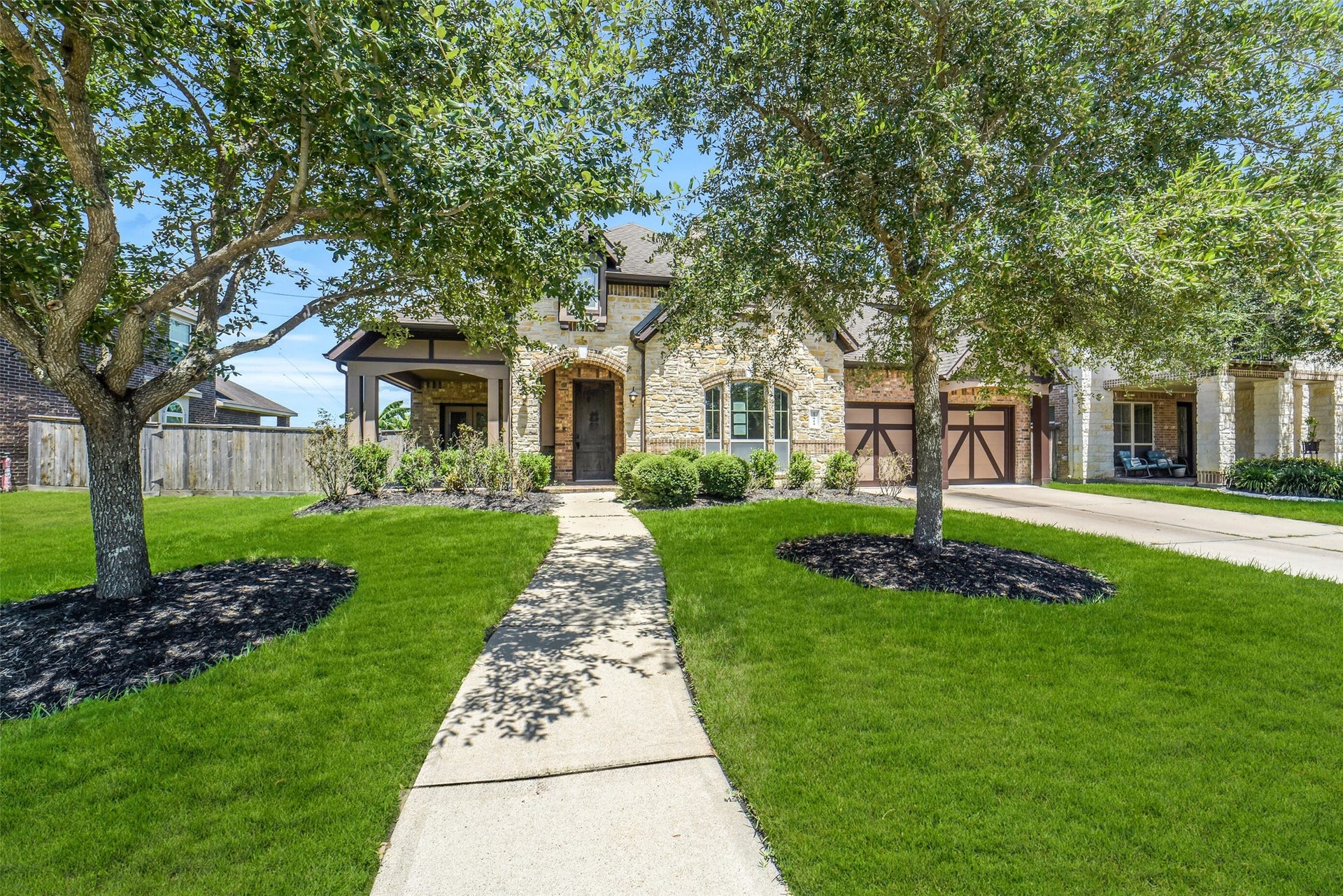 Charming stone facade home with lush landscaping, mature trees, and an inviting pathway leading to a welcoming entrance.