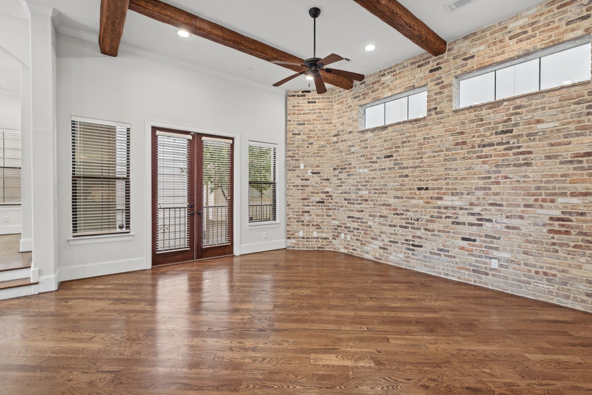 Living Room [16 x 16]  Second Floor. Architectural character takes center stage with exposed wood ceiling beams, rich brick-clad accents, and beautiful natural light. An inviting setting for relaxed evenings or entertaining, where timeless textures lend warmth and distinction.
