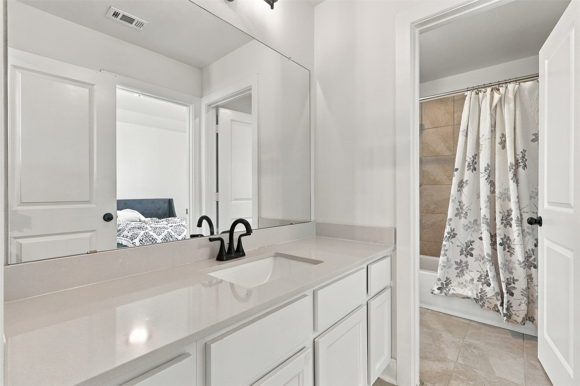 2922 Opal Ivory Way, Richmond, TX 77406 Modern bathroom featuring a sleek vanity with dual sinks, elegant fixtures, and a spacious mirror. The tub-shower combo is complemented by stylish tilework and a floral shower curtain.