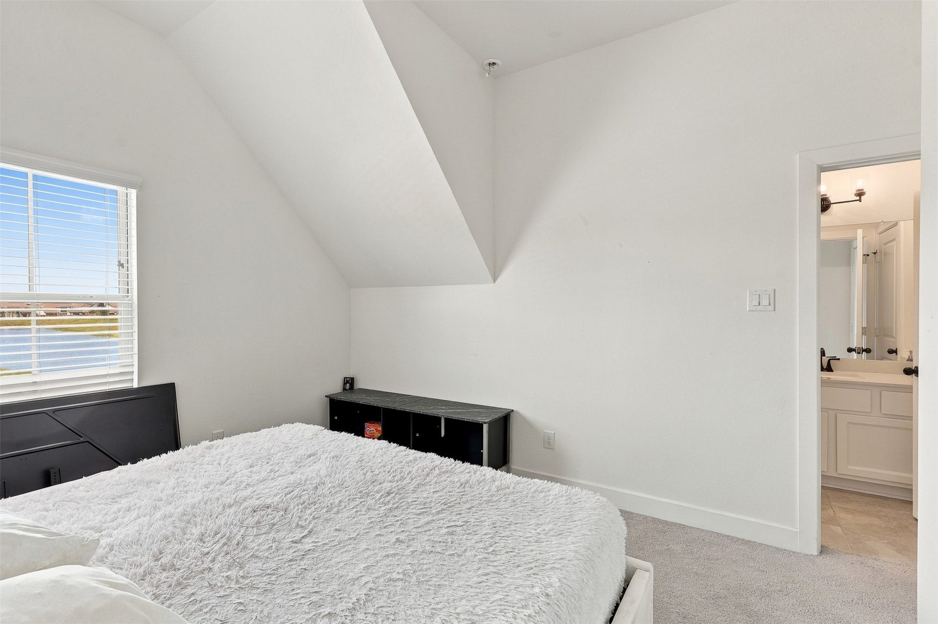 2922 Opal Ivory Way, Richmond, TX 77406 Bright bedroom with a cozy ambiance, featuring a plush bed, angled ceiling, and an ensuite bathroom. A large window offers scenic views and ample natural light.