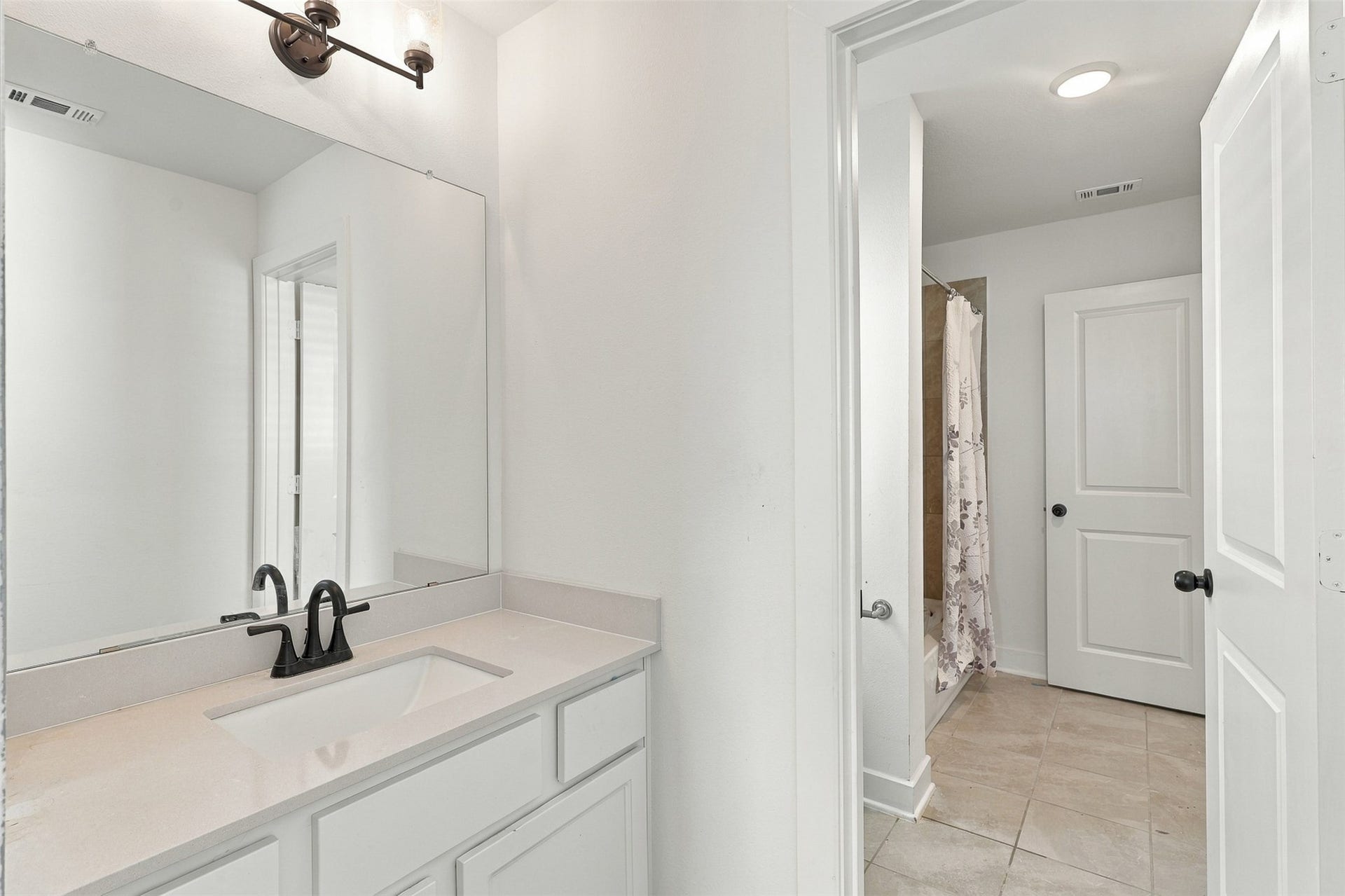 2922 Opal Ivory Way, Richmond, TX 77406 Bright and modern bathroom featuring a sleek vanity with ample storage, elegant black fixtures, and a large mirror, complemented by a tiled shower area.