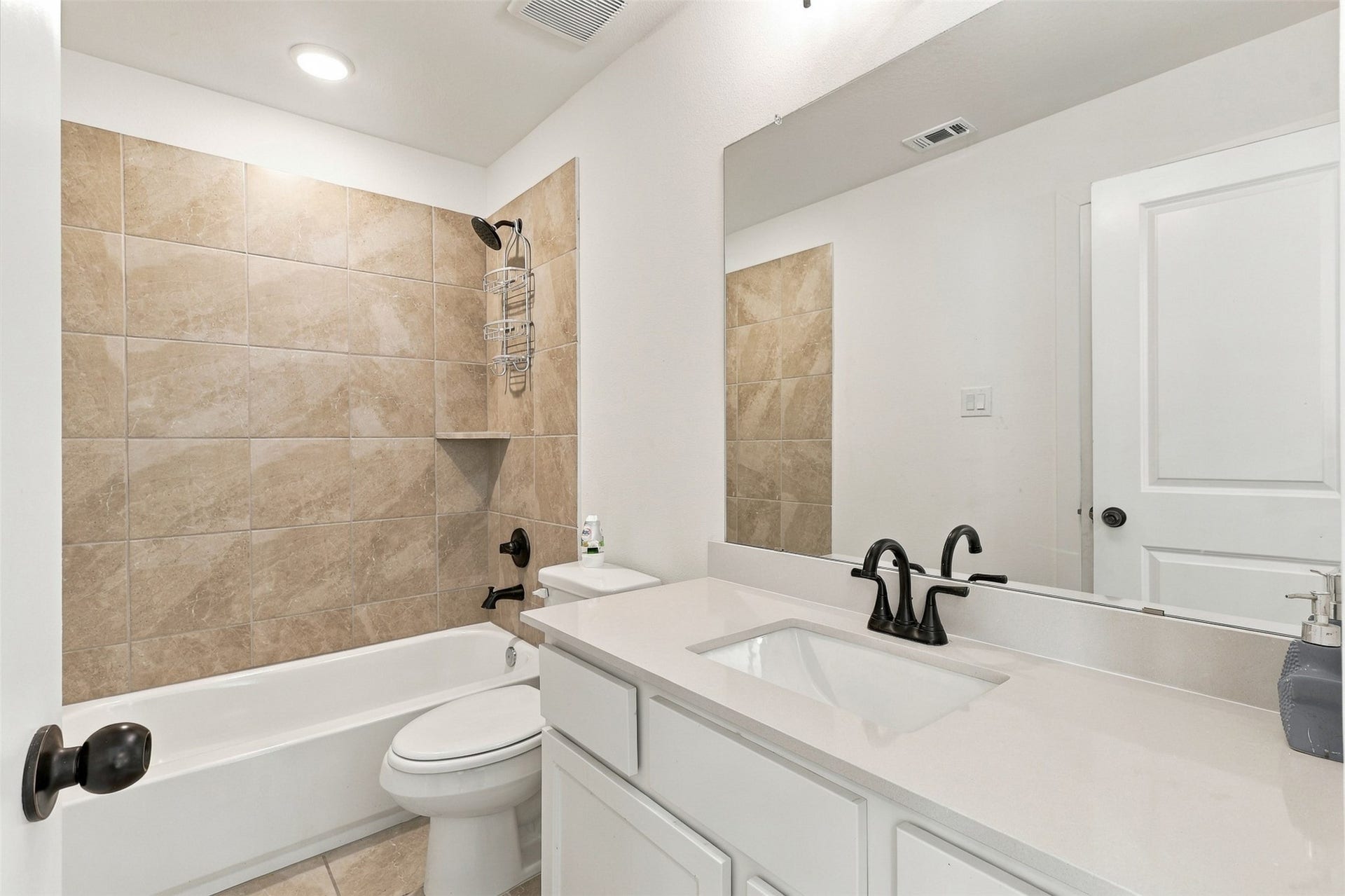 2922 Opal Ivory Way, Richmond, TX 77406 Modern bathroom featuring a sleek white vanity with a black faucet, a spacious mirror, and a bathtub with elegant beige tile surround.