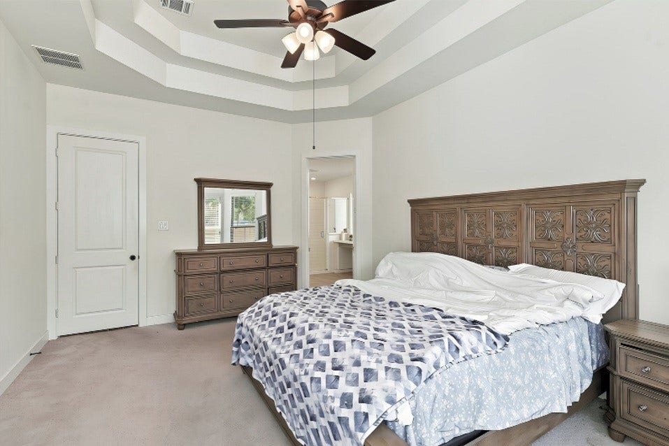 2922 Opal Ivory Way, Richmond, TX 77406 Spacious bedroom with a stylish tray ceiling, featuring a ceiling fan, elegant wooden furniture, and an ensuite bathroom for added convenience.