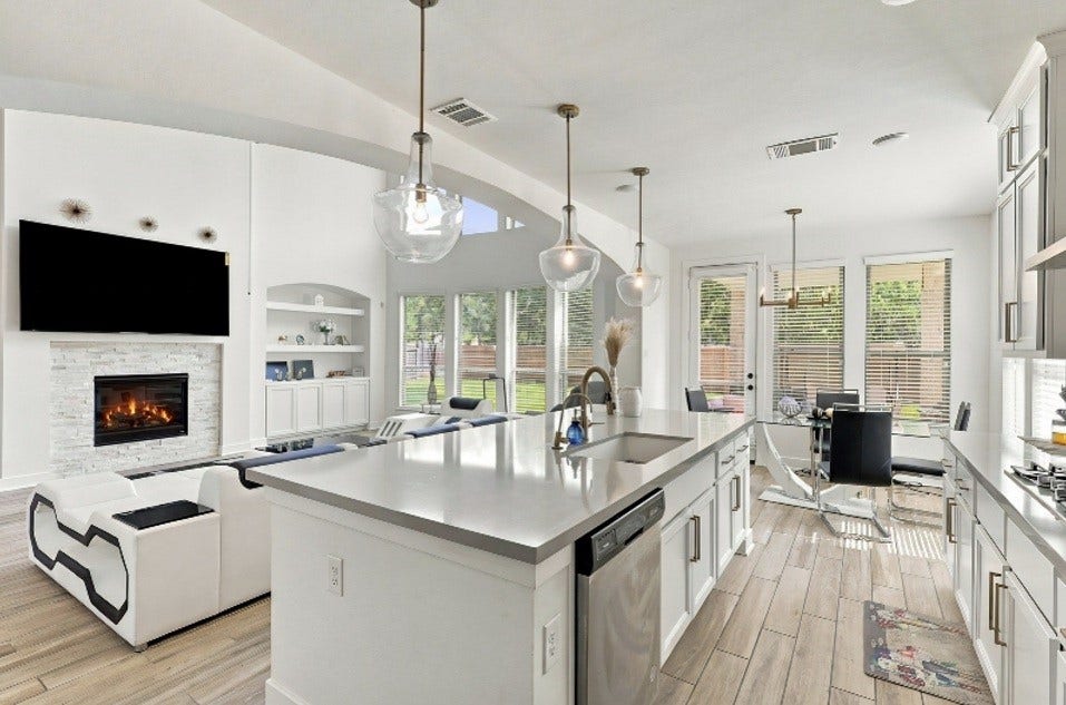 2922 Opal Ivory Way, Richmond, TX 77406 Experience modern elegance in this open-concept living space featuring a sleek kitchen with a large island, pendant lighting, and stainless steel appliances. The adjacent cozy living area boasts a stylish fireplace and abundant natural light from expansive windows, seamlessly connecting to the dining area.