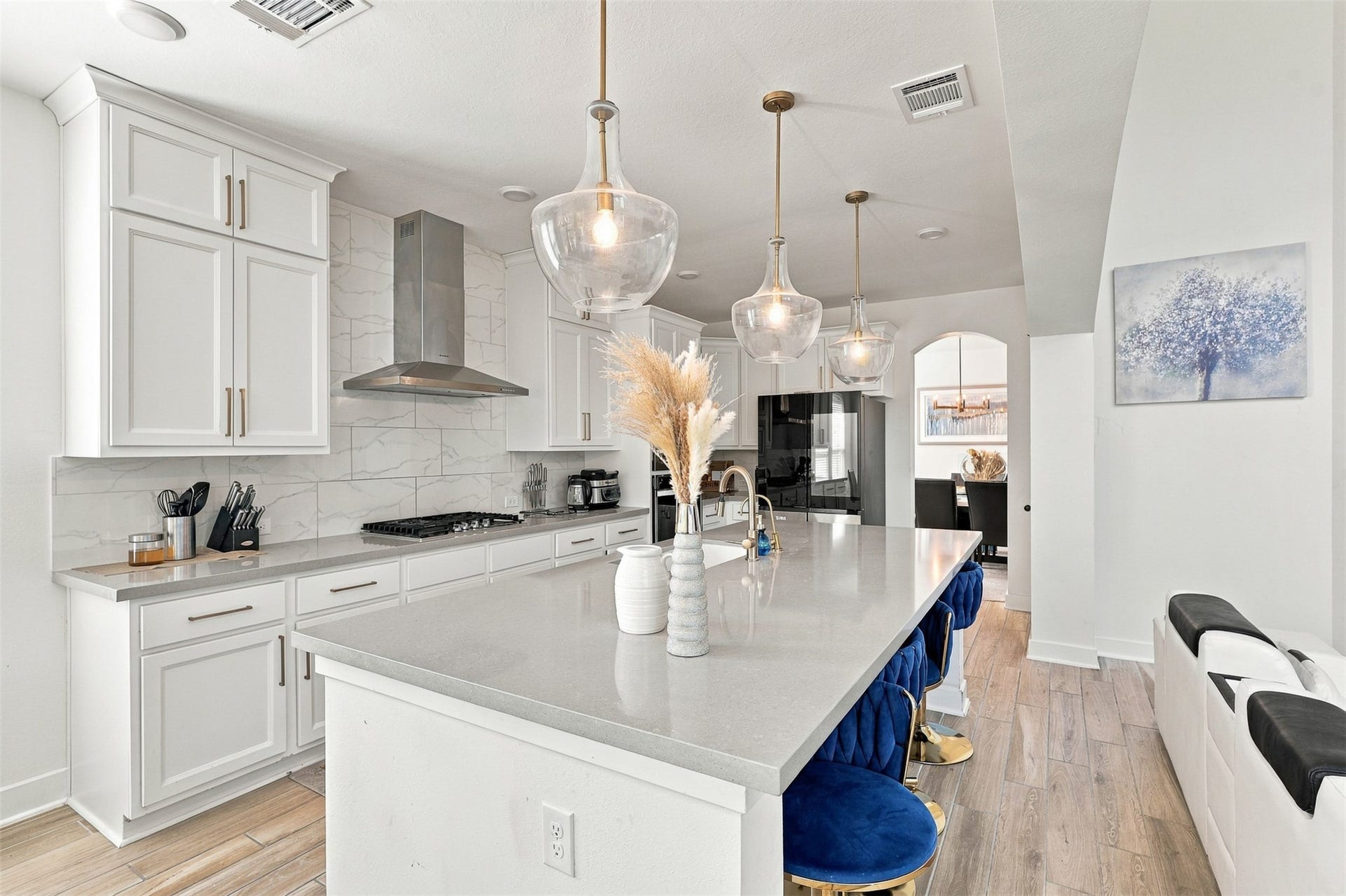 2922 Opal Ivory Way, Richmond, TX 77406 Sleek kitchen with modern white cabinetry, marble backsplash, and a large island featuring pendant lighting and plush blue barstools, perfect for entertaining.