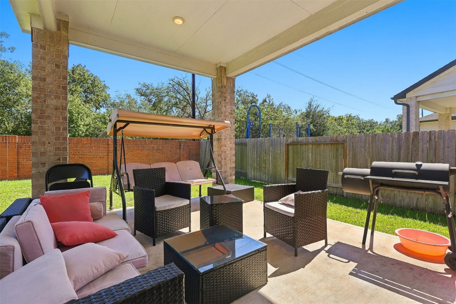 2922 Opal Ivory Way, Richmond, TX 77406 Charming covered patio featuring comfortable seating, a swing for relaxation, and a barbecue grill, perfect for outdoor entertaining in a private fenced yard.