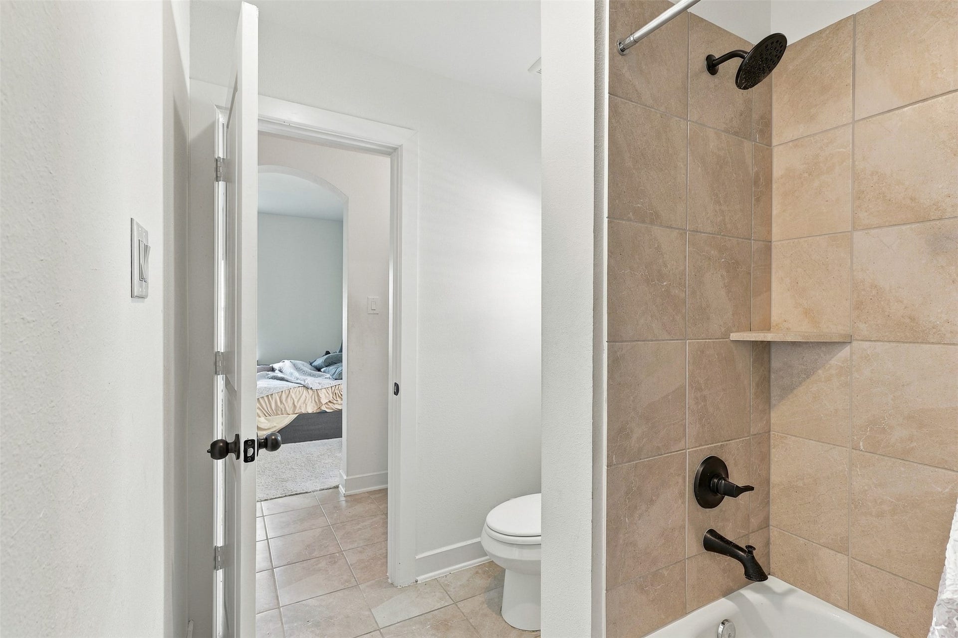 2922 Opal Ivory Way, Richmond, TX 77406 Modern bathroom featuring elegant beige tile work in the shower, complemented by stylish dark fixtures, with a view into a cozy adjacent bedroom.