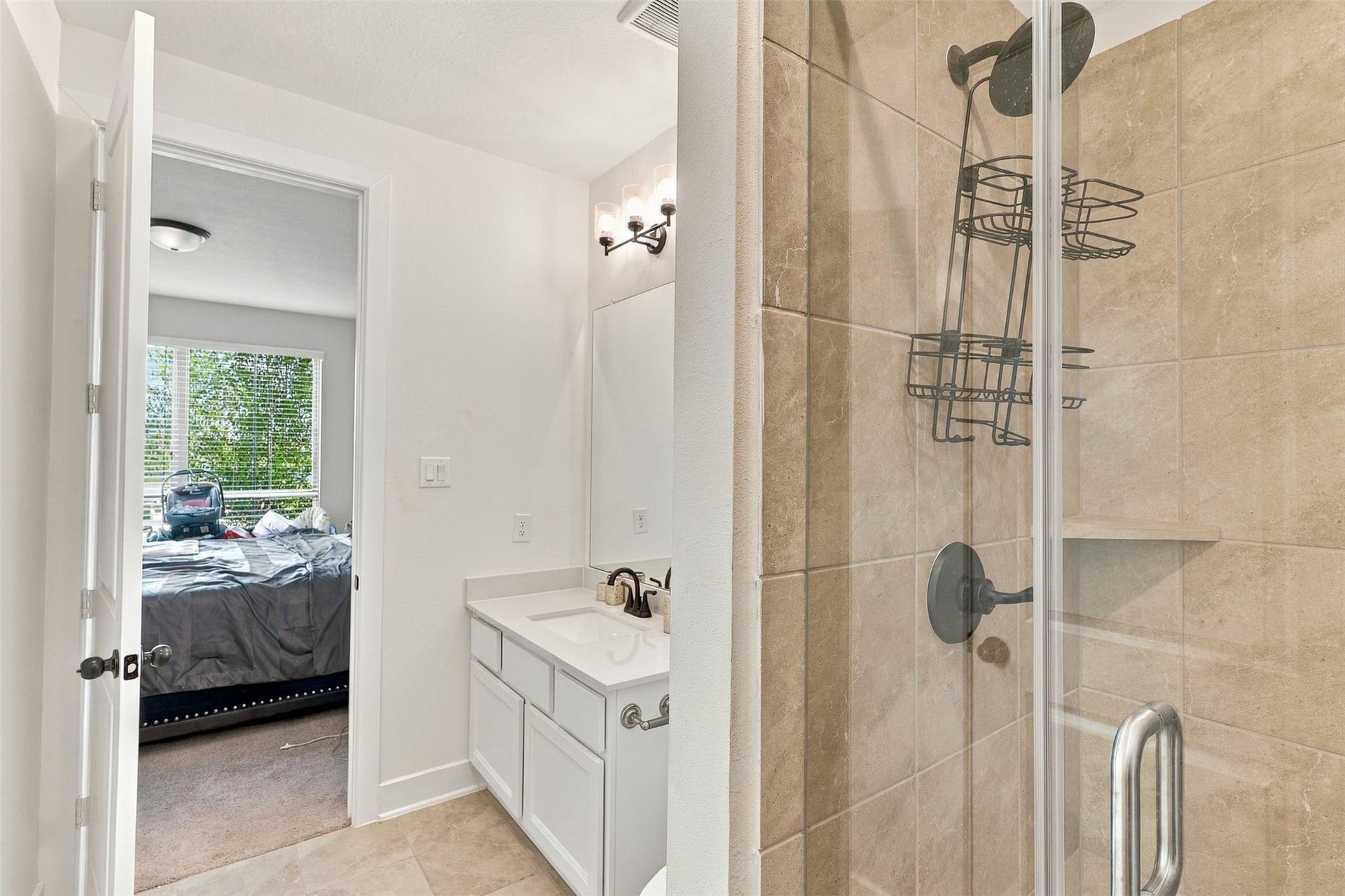 2922 Opal Ivory Way, Richmond, TX 77406 Bright bathroom with a sleek glass shower, elegant tiles, and a spacious vanity. A glimpse into the adjacent bedroom reveals abundant natural light through large windows.