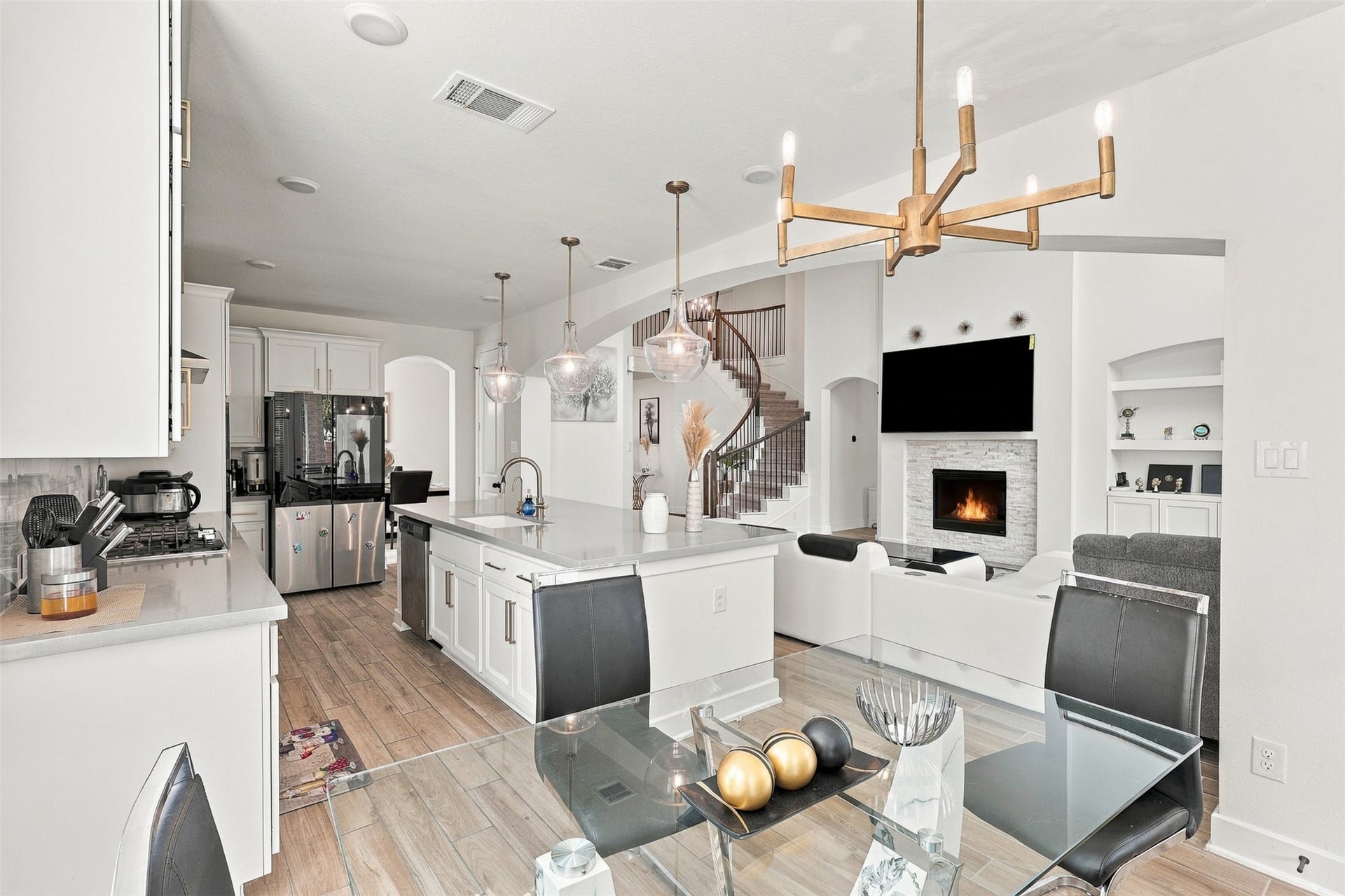 2922 Opal Ivory Way, Richmond, TX 77406 Elegant open-concept living space featuring a modern kitchen with a central island, stylish pendant lighting, and a cozy living area with a fireplace and large TV, perfect for entertaining.
