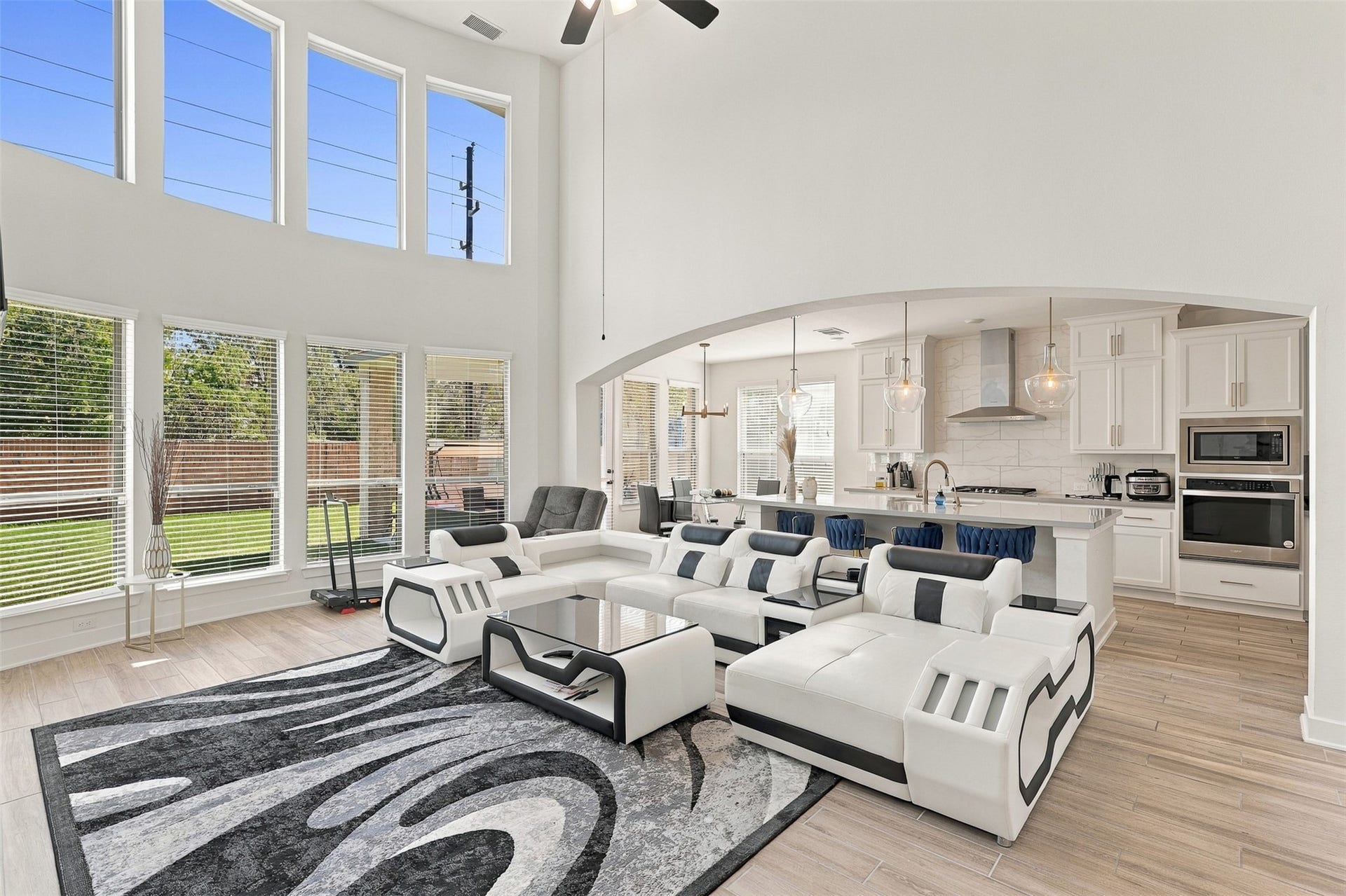 2922 Opal Ivory Way, Richmond, TX 77406 Spacious and bright living area with soaring ceilings and large windows, seamlessly flowing into a modern kitchen featuring sleek white cabinetry, stainless steel appliances, and a chic breakfast bar.