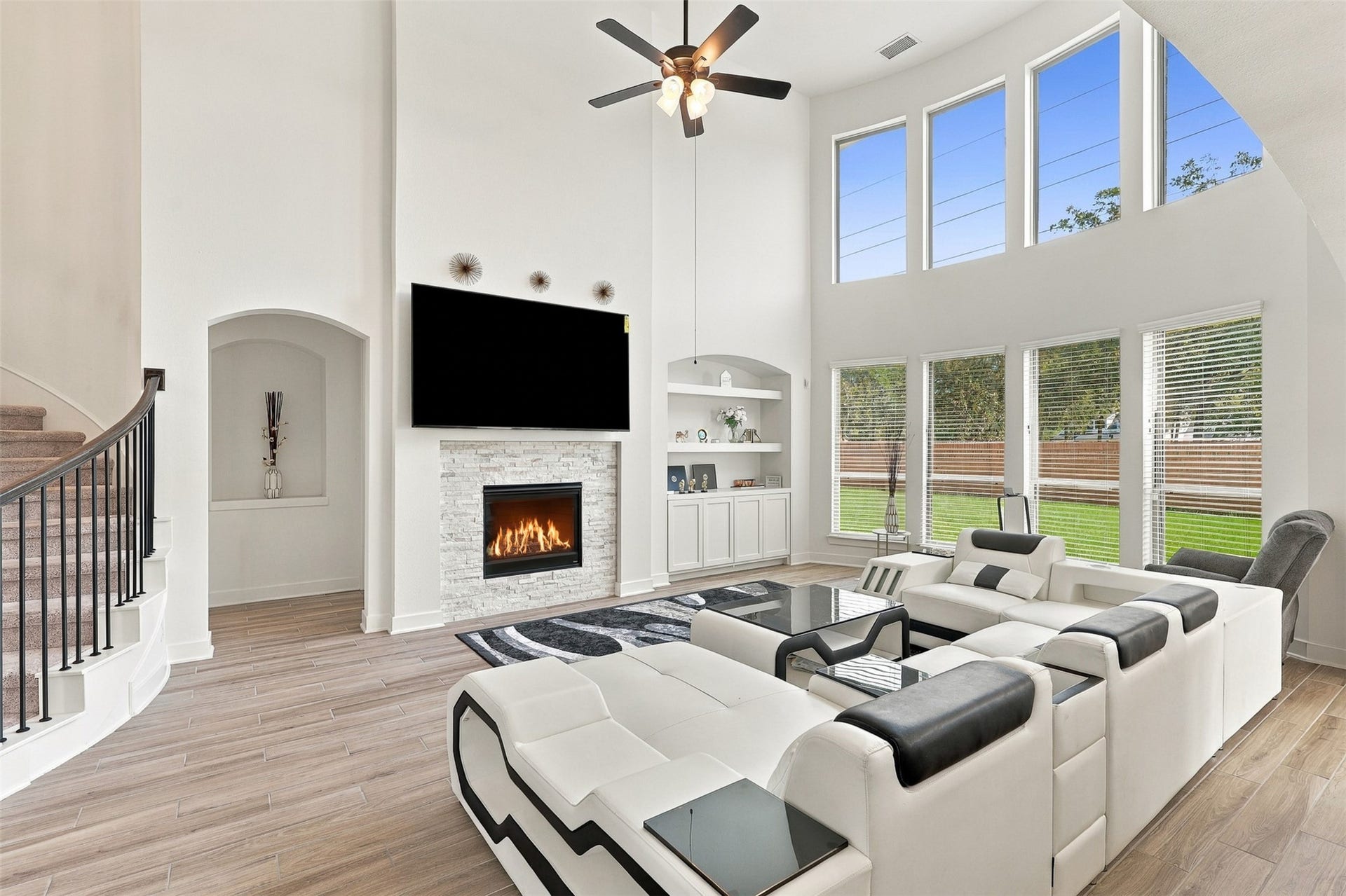 2922 Opal Ivory Way, Richmond, TX 77406 Spacious living room with soaring ceilings, large windows providing abundant natural light, and a cozy fireplace. Modern design features a stylish staircase and sleek flooring, perfect for relaxation and entertainment.