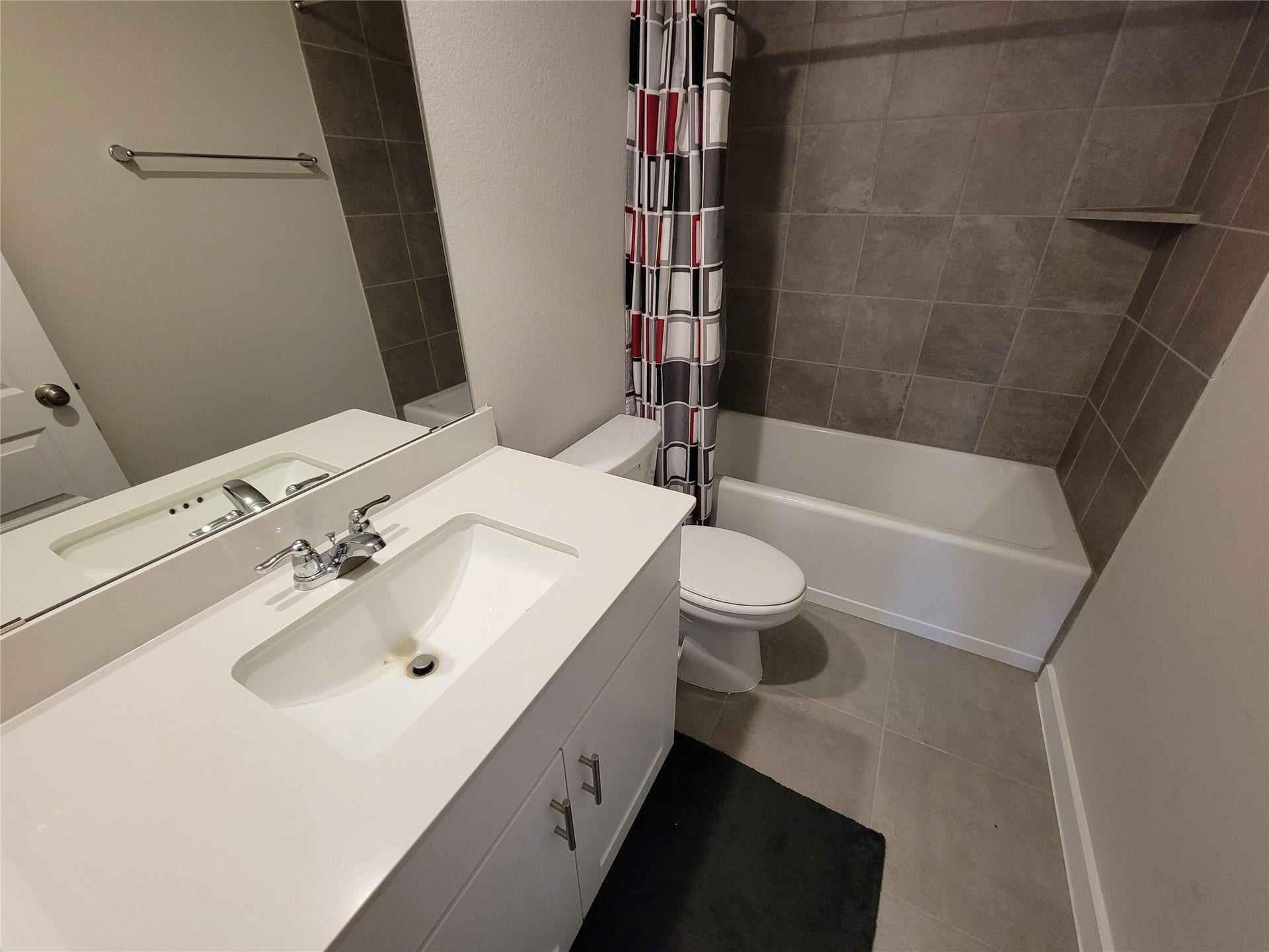 10843 Bodie Hills Drive, Rosharon, TX 77583 Modern bathroom with sleek white vanity, elegant tile flooring, and a stylish shower-tub combo featuring contemporary patterned curtains.